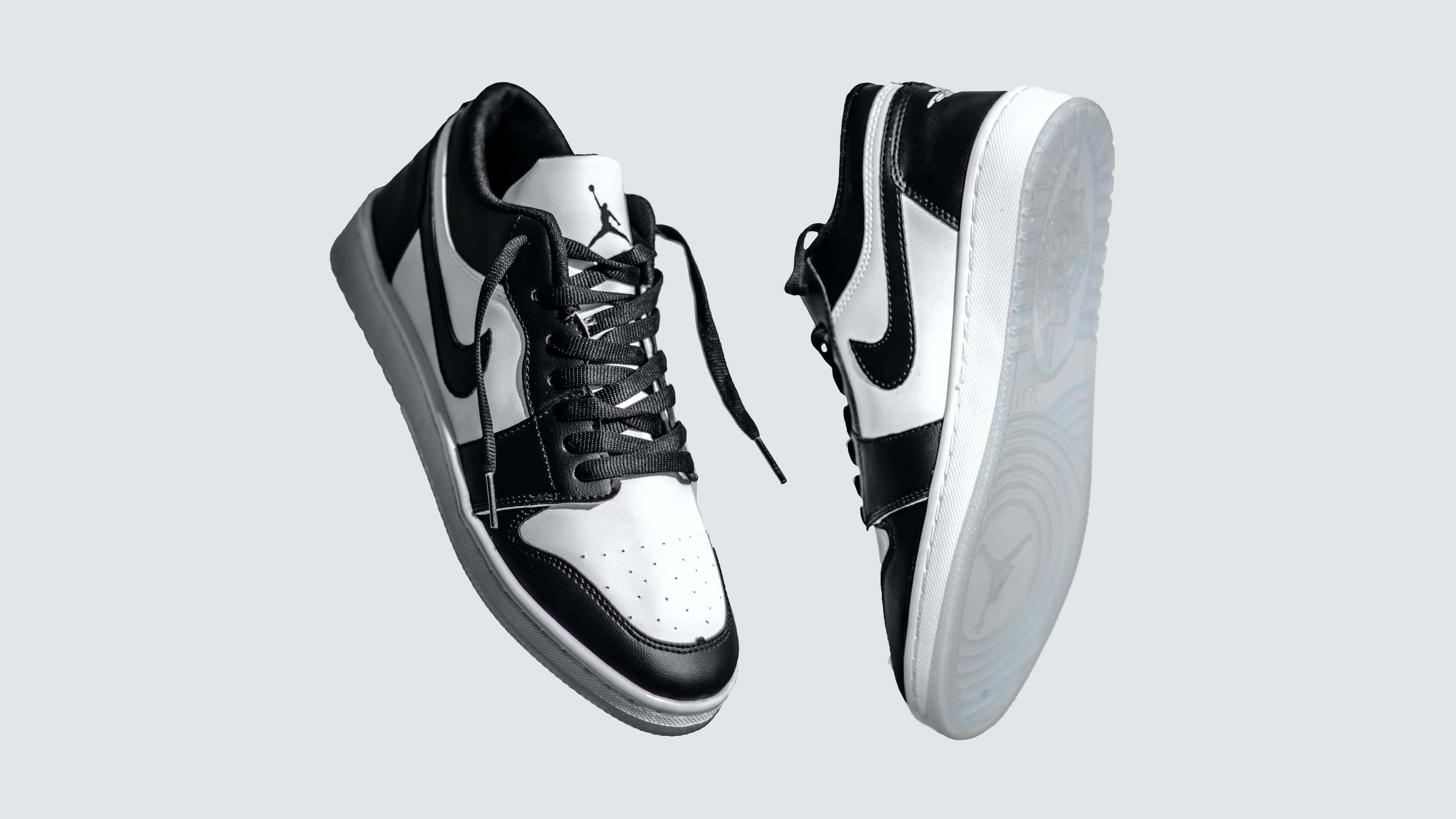 穿著Air Jordan鞋款，展現時尚風采 4K 壁紙 — 兩對黑白Jordan運動鞋漂浮在淺灰色背景上，展示其標誌性設計和鞋底圖案。