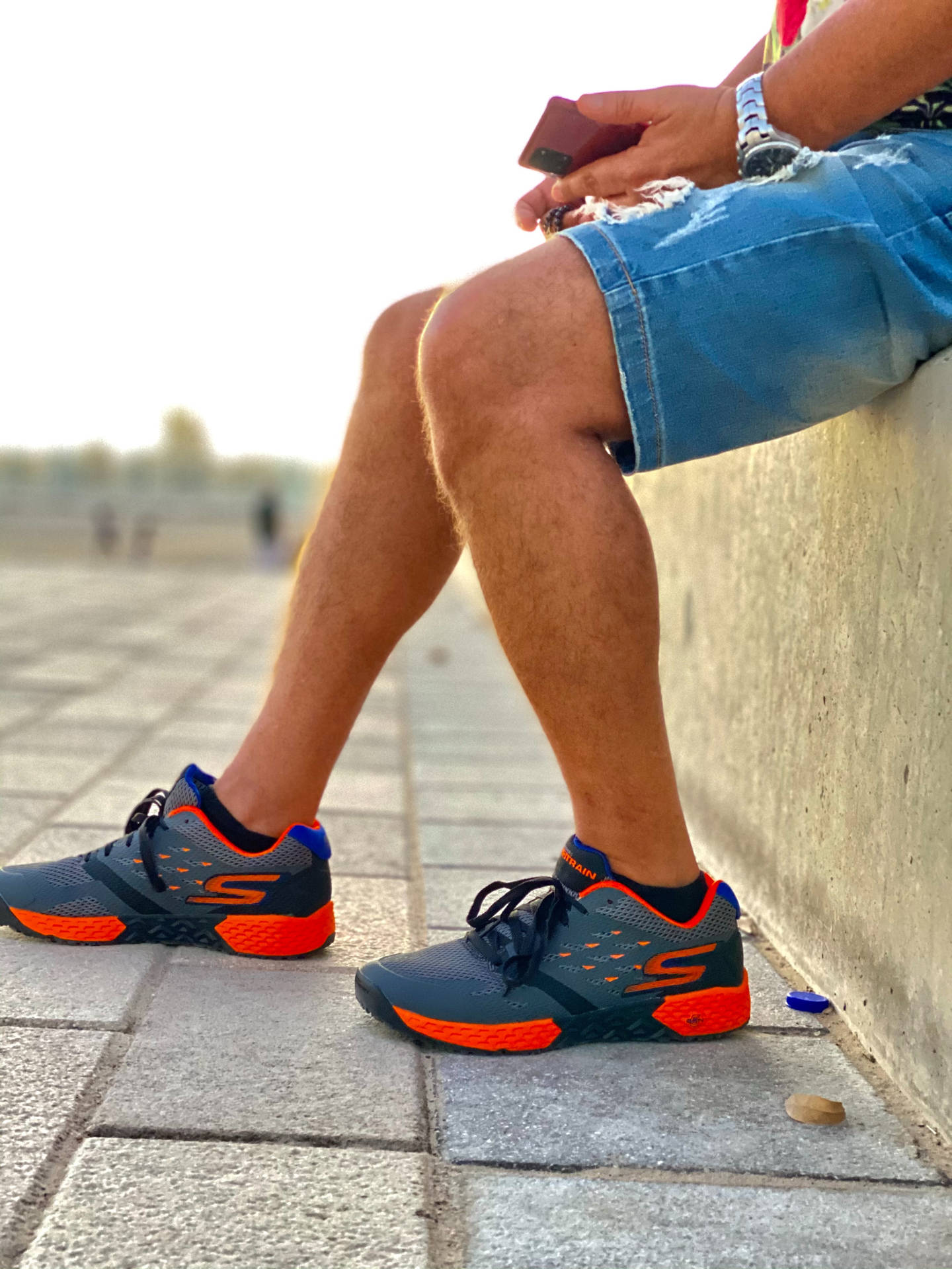 穿著運動鞋的人坐在石牆上，手裡拿著手機。
