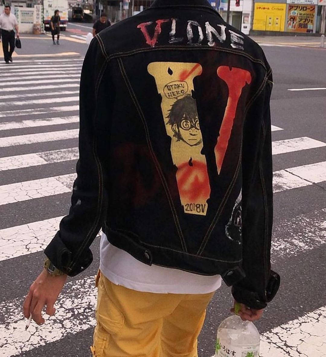 Vlone 桌布 壁紙 — 穿著印有大型動漫圖案黑色牛仔褸的人，從背面看正在穿過城市行人過路處。