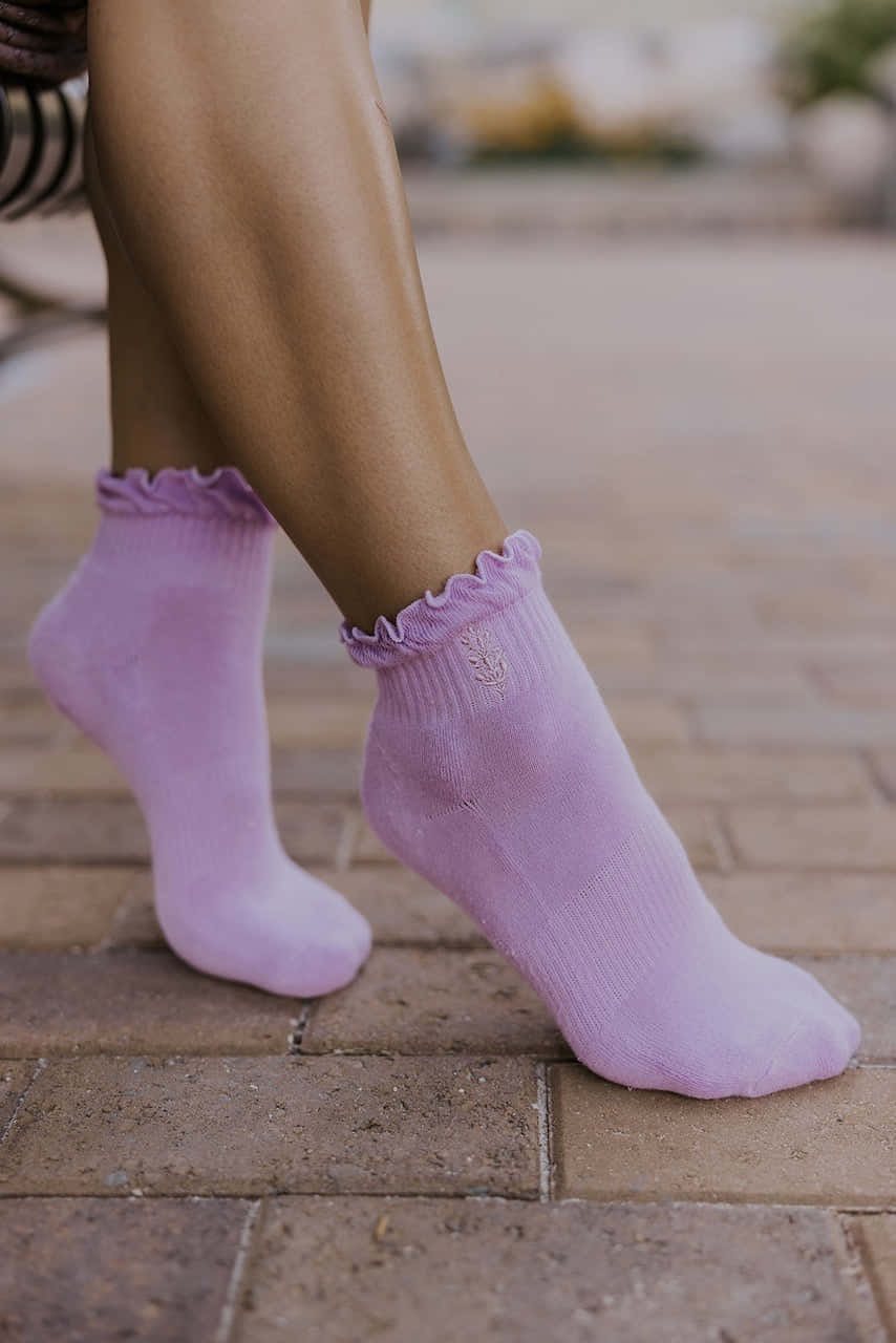 Purple Socks 桌布 壁紙 — 穿著柔軟薰衣草色襪子、帶荷葉邊袖口的腿部特寫，站在磚砌庭院上。