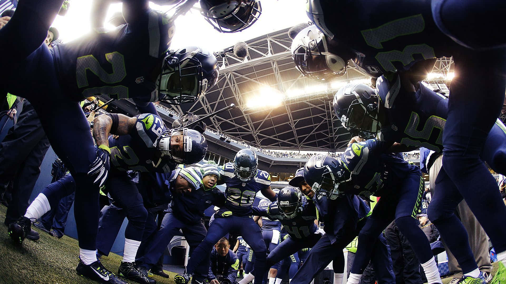 NFL 桌布 壁紙 — 穿著海鷹隊球衣的足球運動員在球場燈光下，在明亮的場地上緊密地圍成一圈。