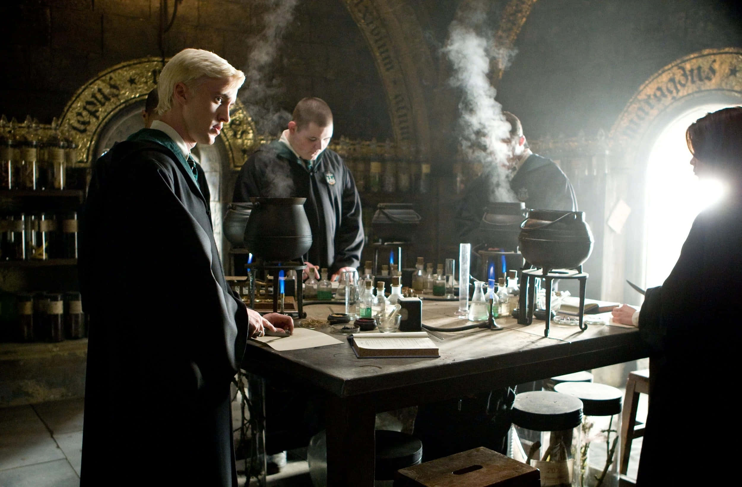 The Hogwarts Potions Class 桌布 壁紙 — 穿著深色長袍的學生在光線昏暗、充滿蒸氣的教室裡釀造藥水，教室裡有拱形窗戶和裝滿玻璃罐的架子。