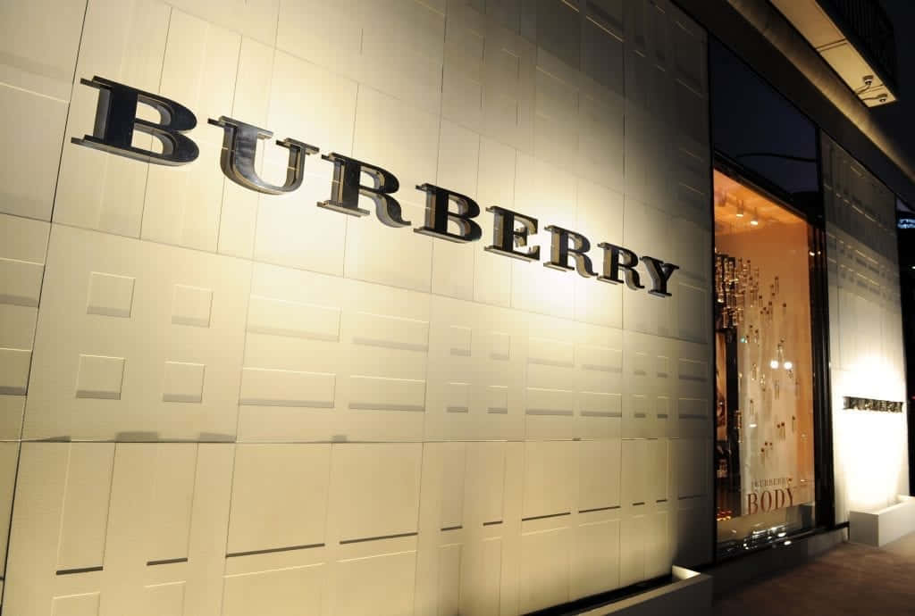 穿著真誠 Burberry 時尚，展現品味 壁紙 — 夜間時尚的 Burberry 商店外牆，帶有發光標誌和帶紋理的白色面板，投射出柔和陰影。
