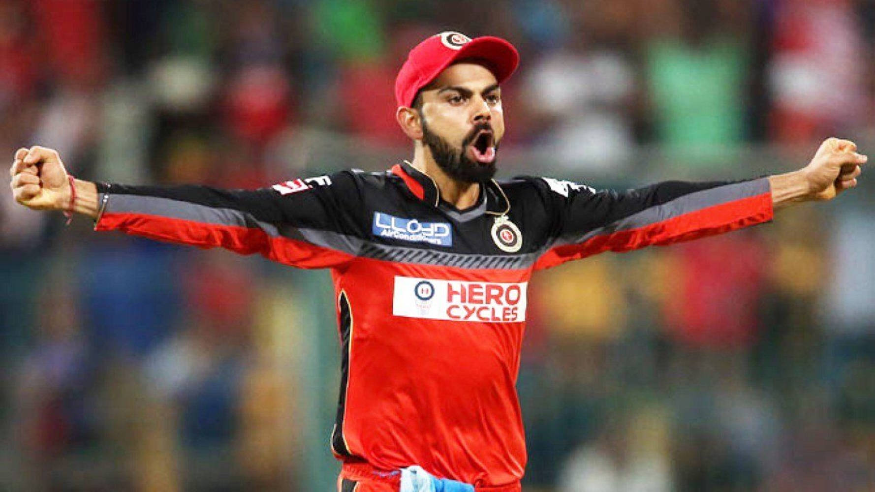 virat kohli rcb 桌布 壁紙 — 穿著紅色球衣的板球運動員在明亮的燈光下於球場張開雙臂、張開嘴巴慶祝。