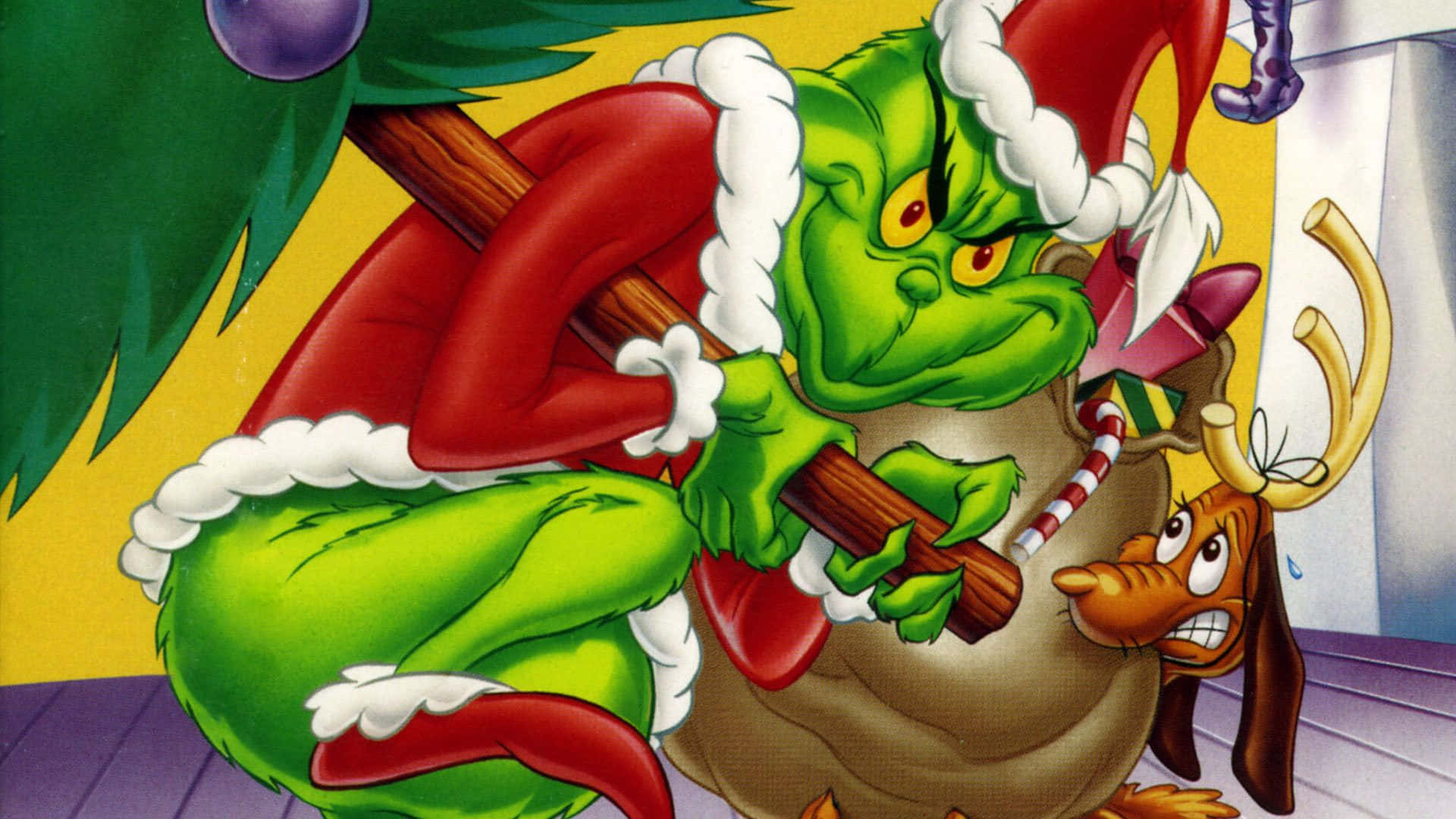 The Grinch 桌布 壁紙 — 穿著紅色聖誕老人服飾、帶白色飾邊的鬼靈精拿著一個袋子和一根拐杖糖，一隻受驚的狗在聖誕樹旁看著。