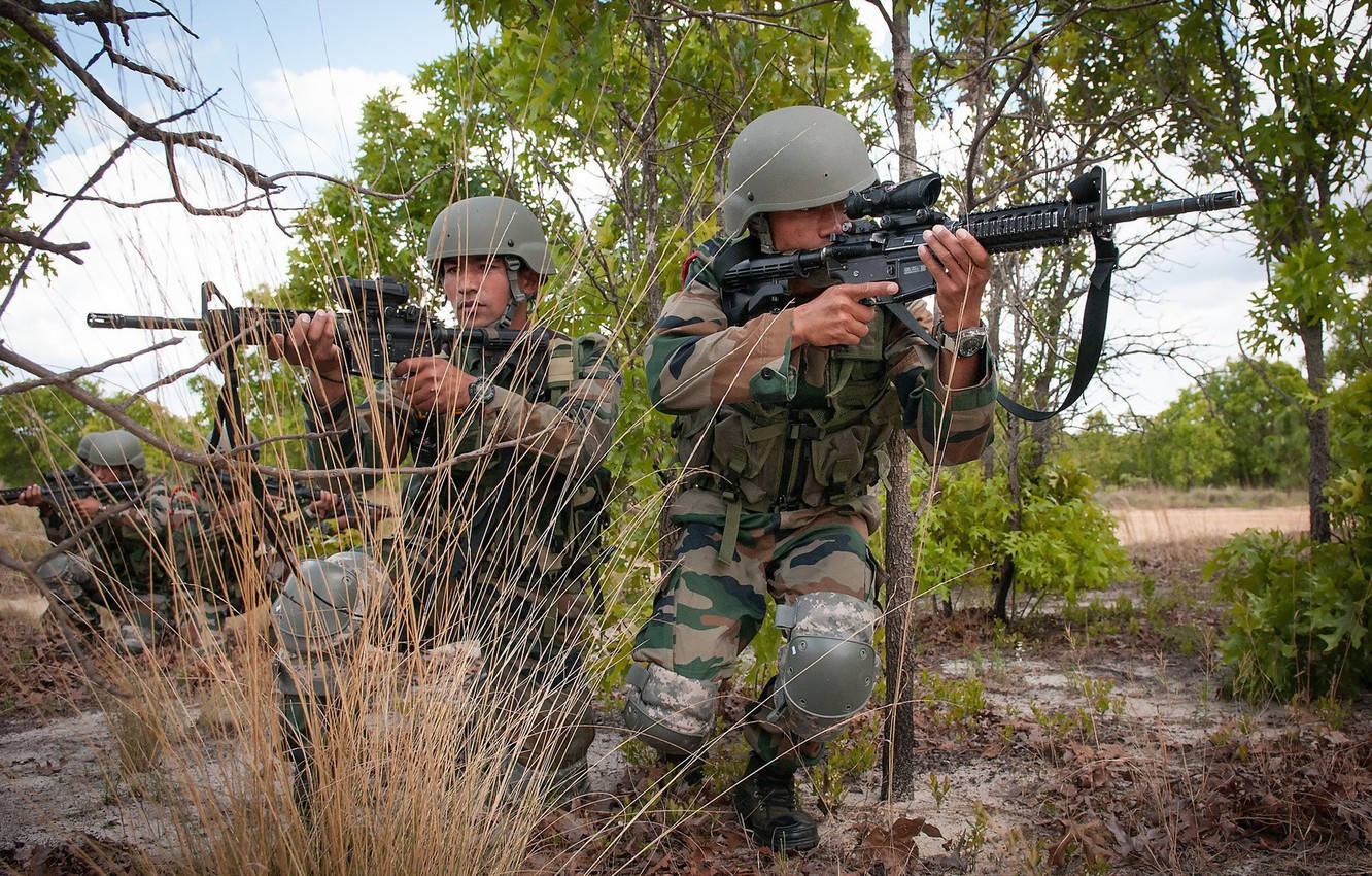 Indian Army 桌布 壁紙 — 穿著迷彩裝備的士兵在乾燥的林地訓練中蹲在高草和樹木後面瞄準步槍。