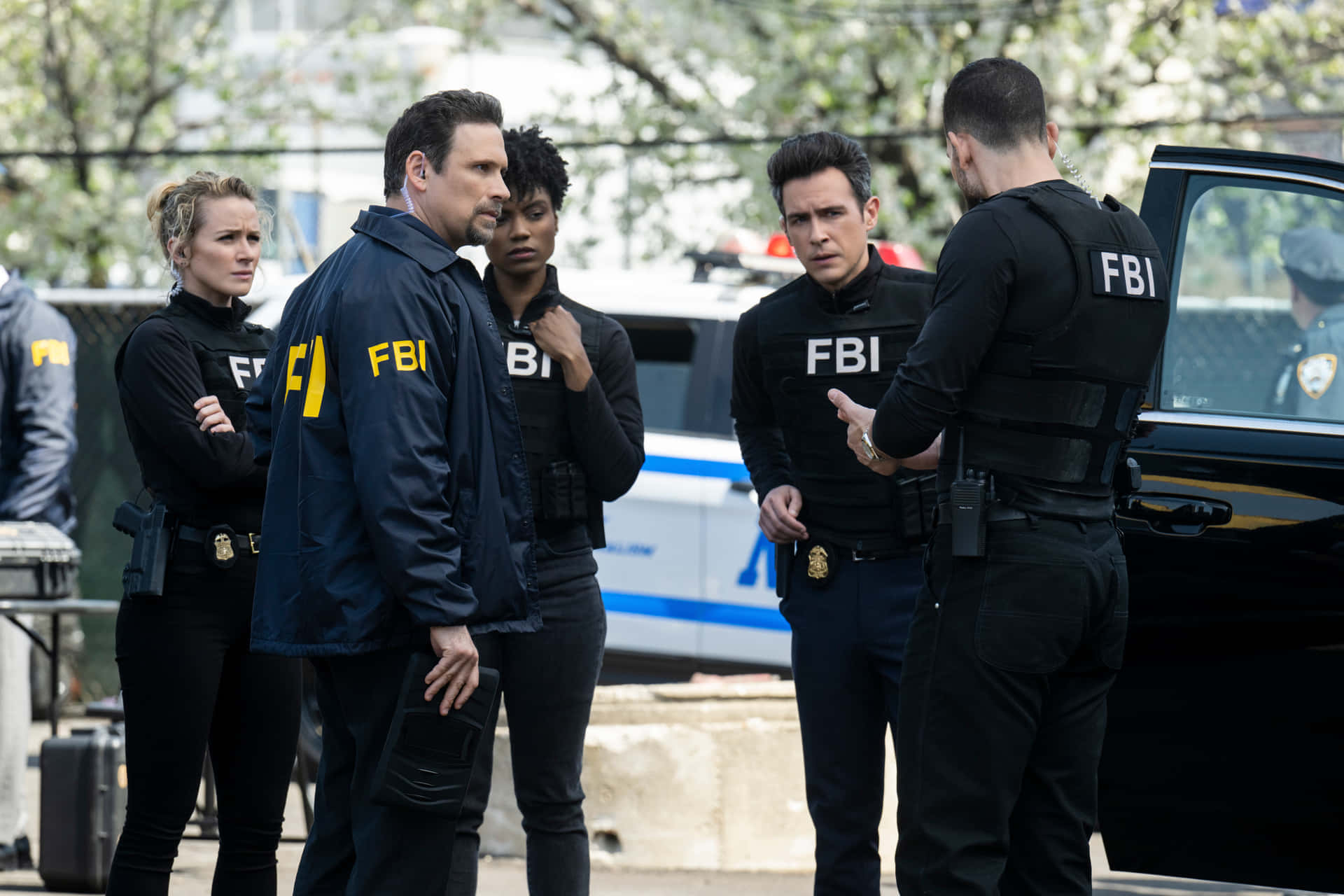 Fbi 桌布 壁紙 — 穿著黑色戰術裝備的FBI探員在城市環境中，於警車附近進行緊張討論。
