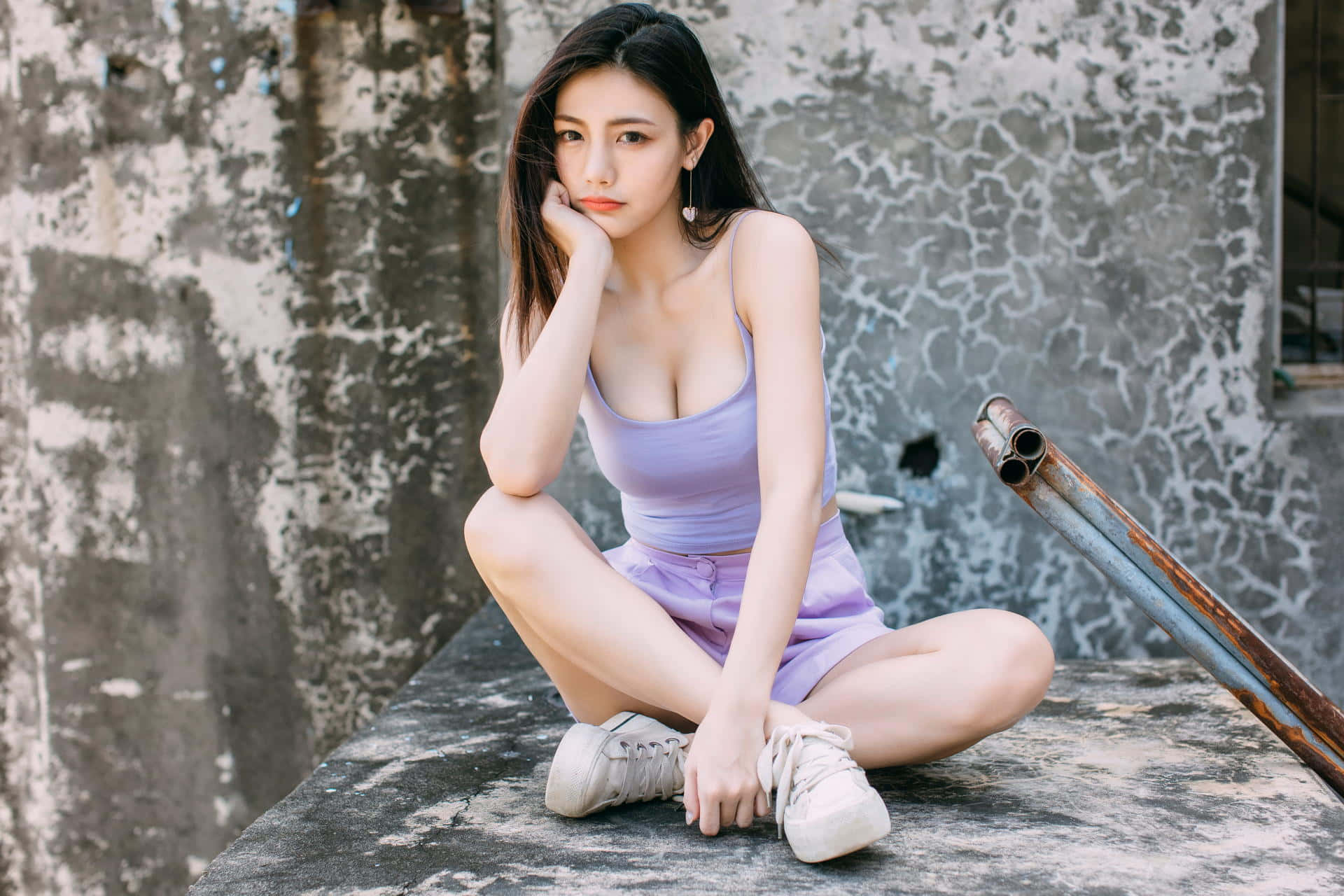 身穿薰衣草色服裝的年輕女性，靠著裂縫牆壁坐在混凝土邊緣上。