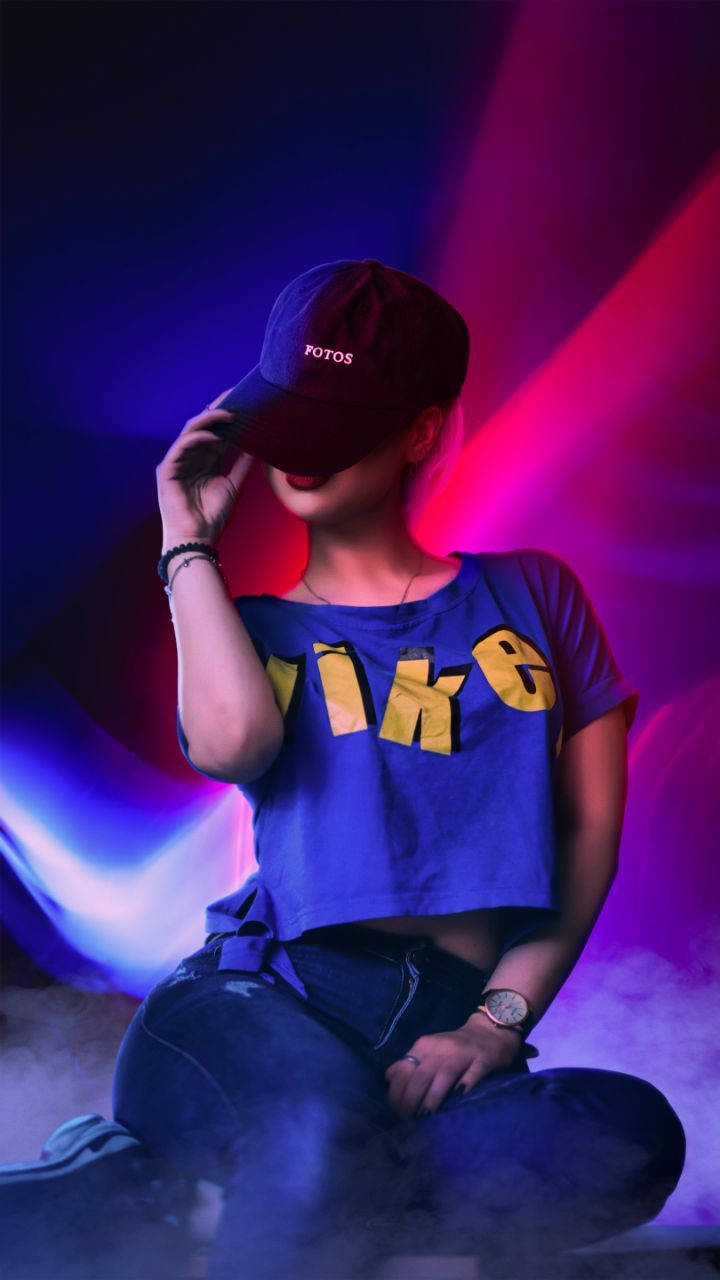 穿藍色Nike上衣的手機女孩 壁紙 — 一個身穿藍色Nike短版上衣和帽子的人坐在充滿活力的紫色和粉紅色霓虹燈光中，煙霧在他們周圍繚繞。