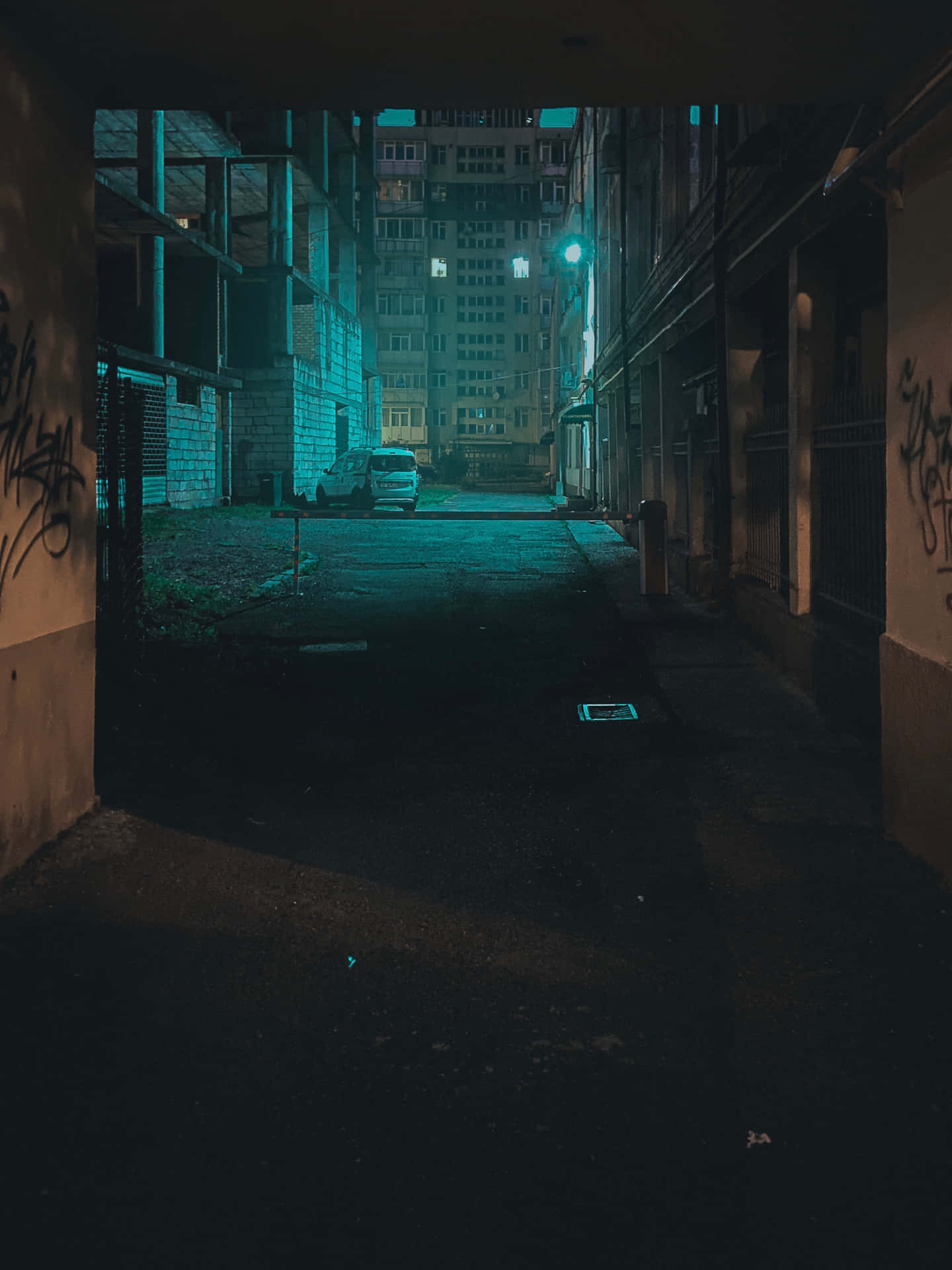夜晚黑暗的城市小巷，帶有青綠色照明和塗鴉覆蓋的牆壁。