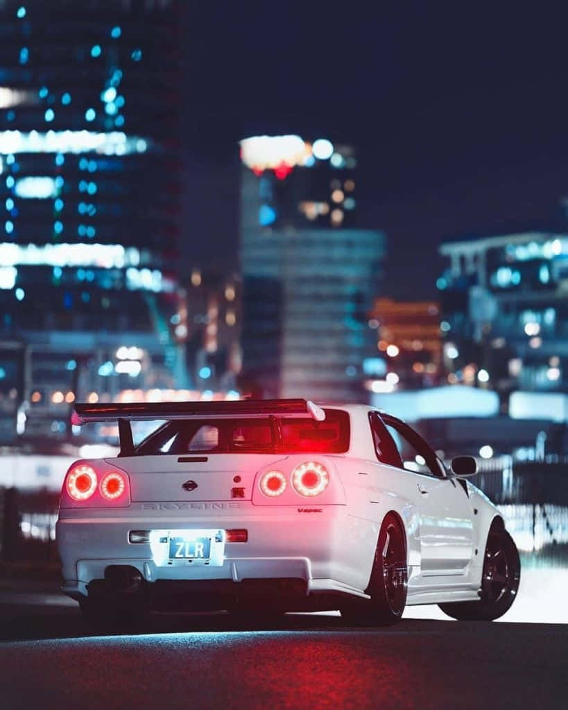 夜晚潮濕城市街道上的白色日產Skyline R34跑車，帶有發光的紅色尾燈。