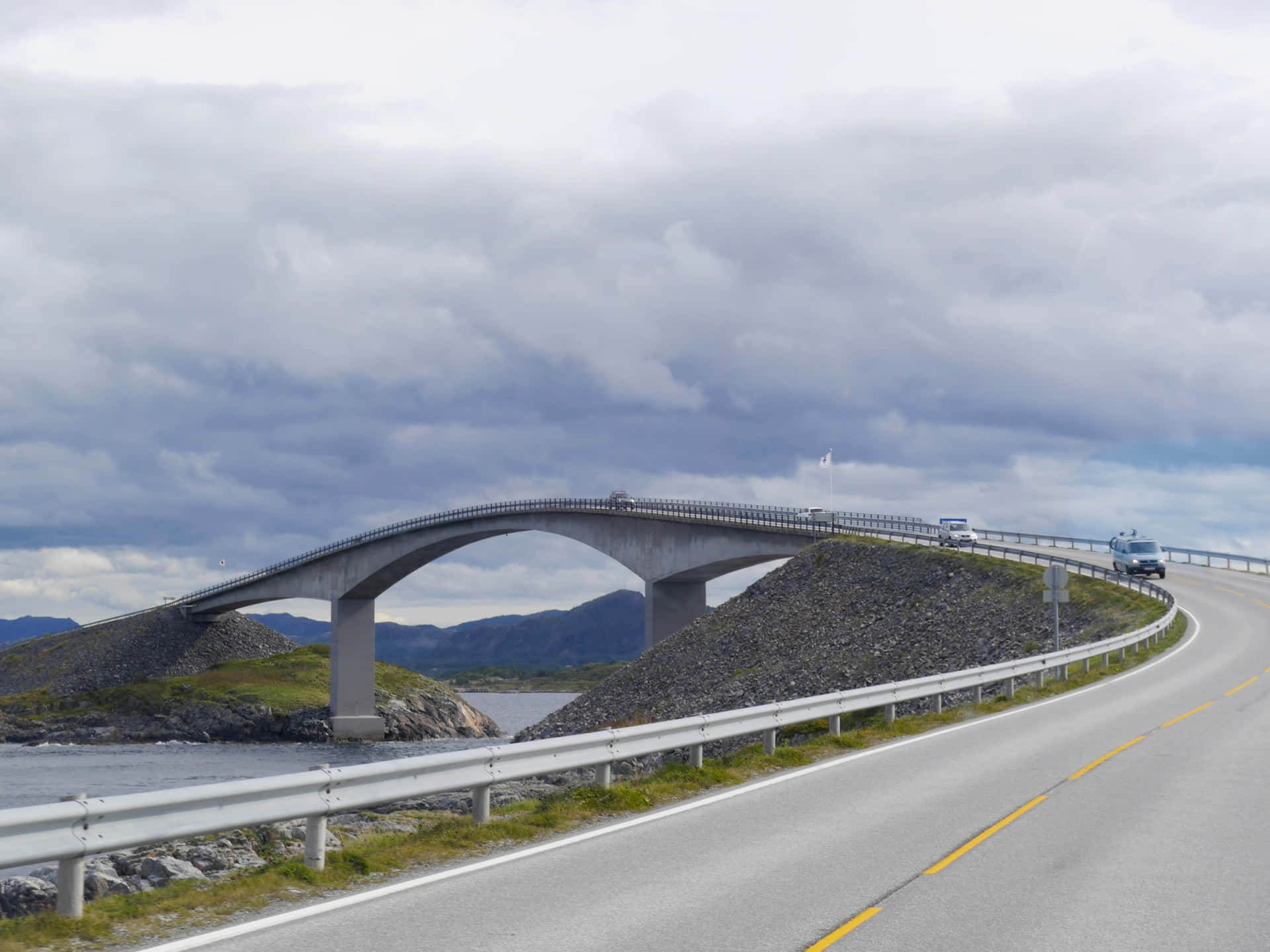 一座彎曲的混凝土橋橫跨岩石峽灣，車輛在蜿蜒的道路上行駛，天空多雲。