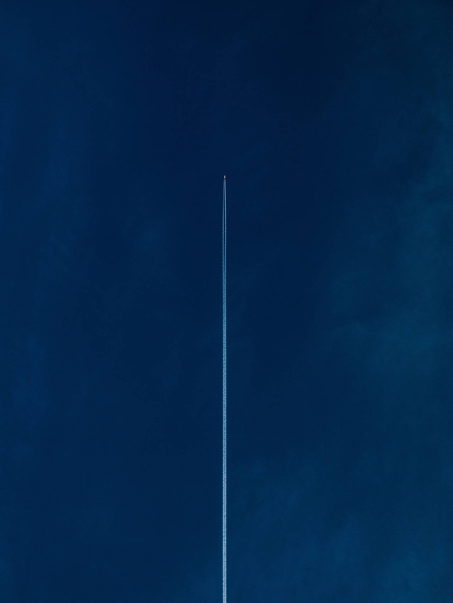 一架飛機高飛，在深藍色的天空中留下一道長長的白線。