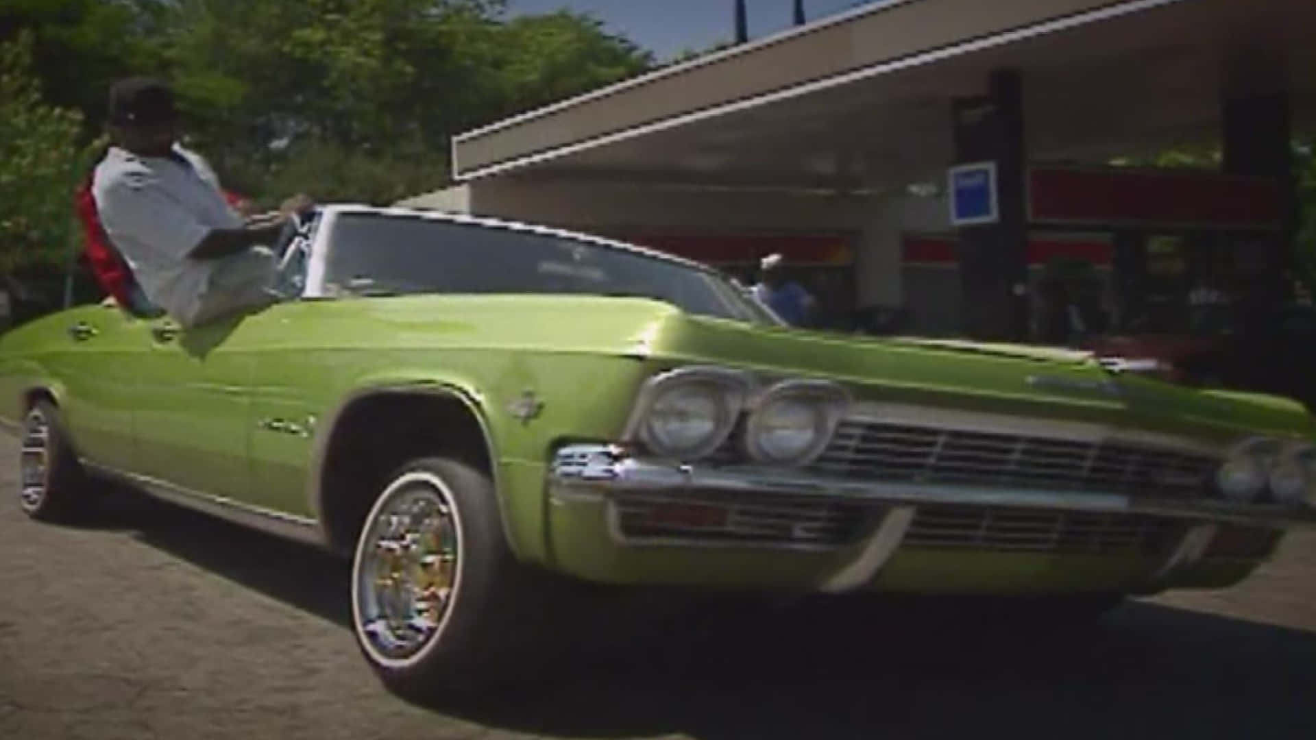 穿越時光：90年代經典 Freaknik 壁紙 — 一輛充滿活力的青檸綠色經典敞篷車停在加油站，司機座位上坐著一名男子。