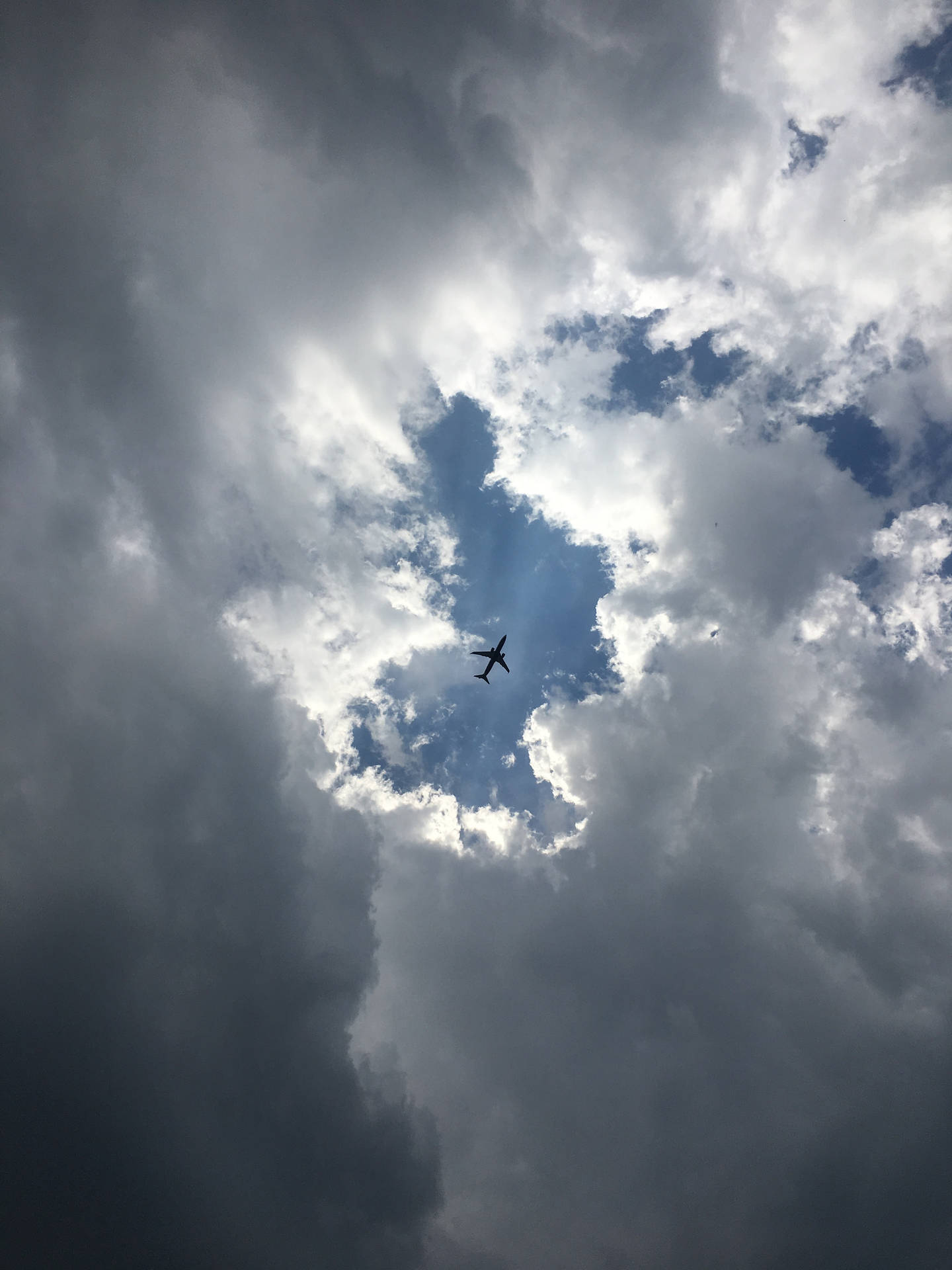 一架孤獨的飛機飛過戲劇性的多雲天空，帶有藍色斑塊。