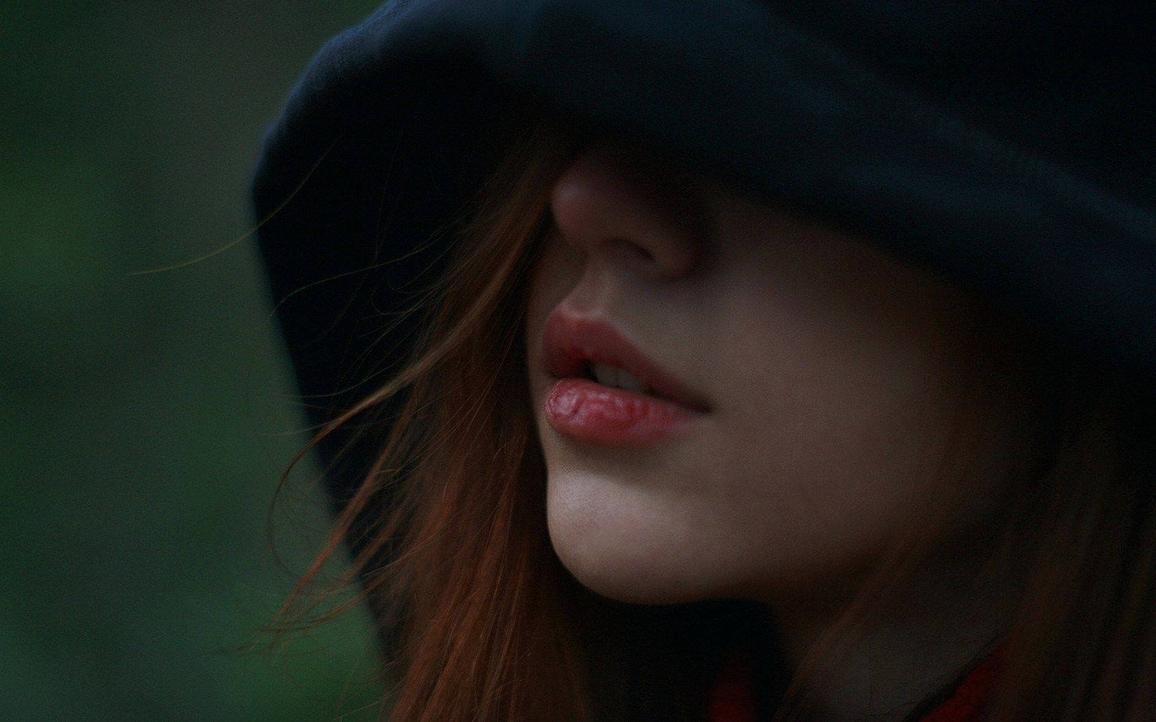 一個女人喺深色兜帽下嘅嘴唇同下巴，紅髮。