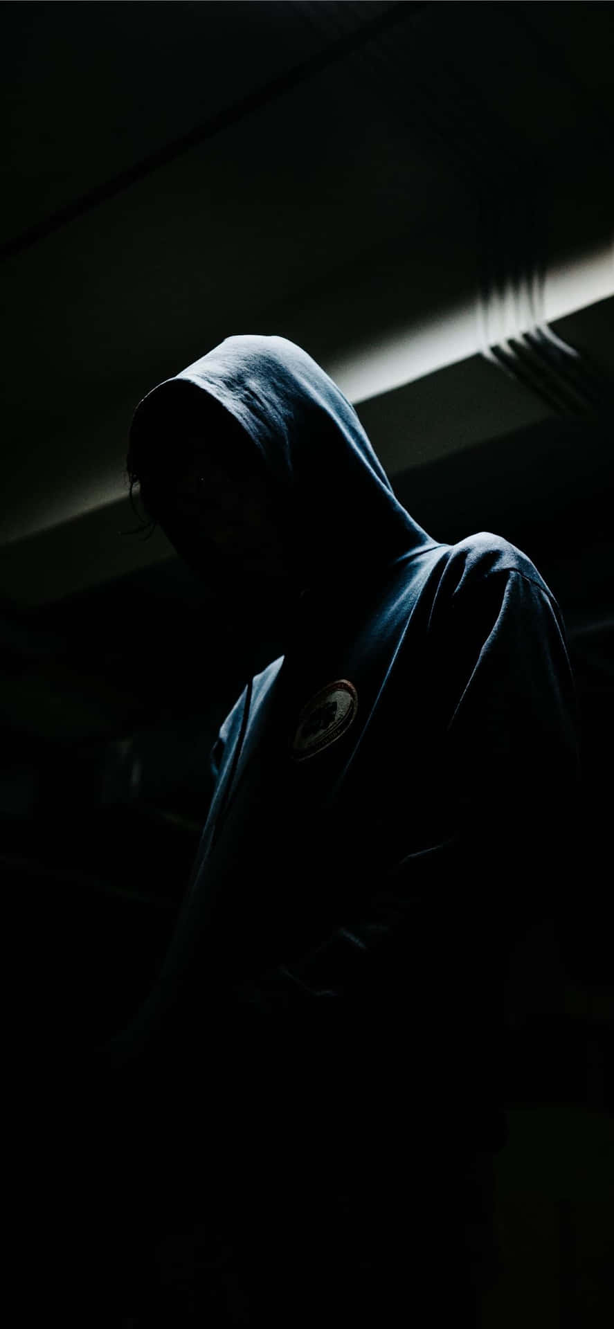 一個穿著深色連帽衫的人站在陰影中，光線極少。 — 傷心 壁紙