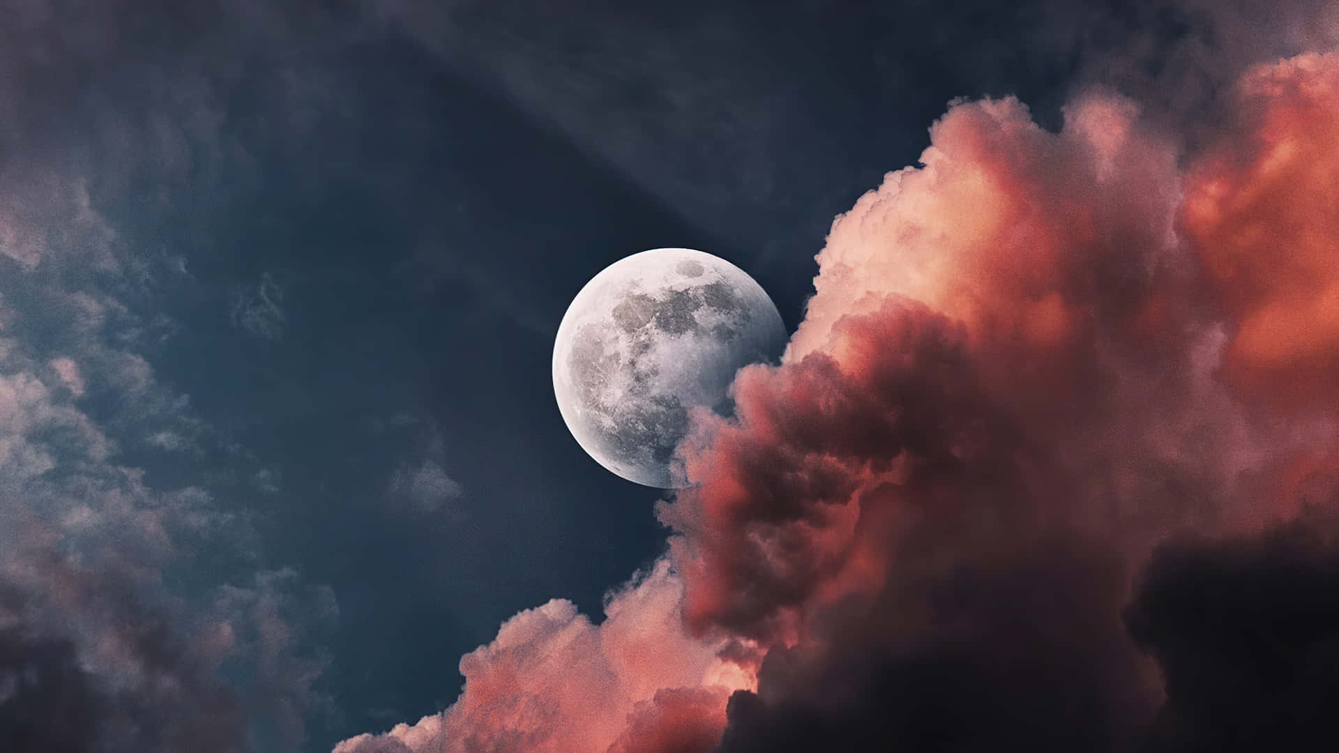 滿月在夜間多彩雲層後升起。