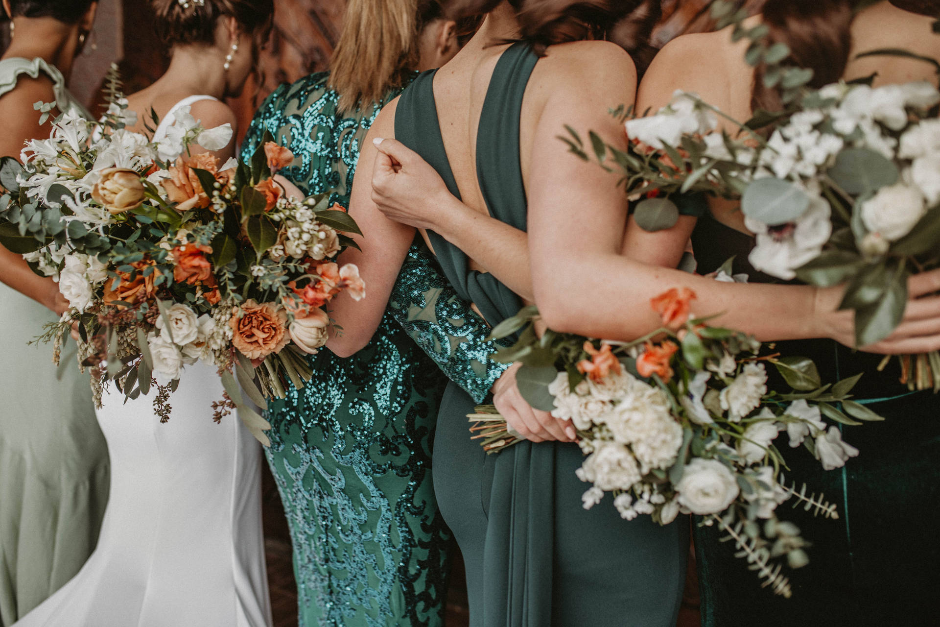 一群身穿綠色和白色裙子的伴娘拿著花束擁抱。