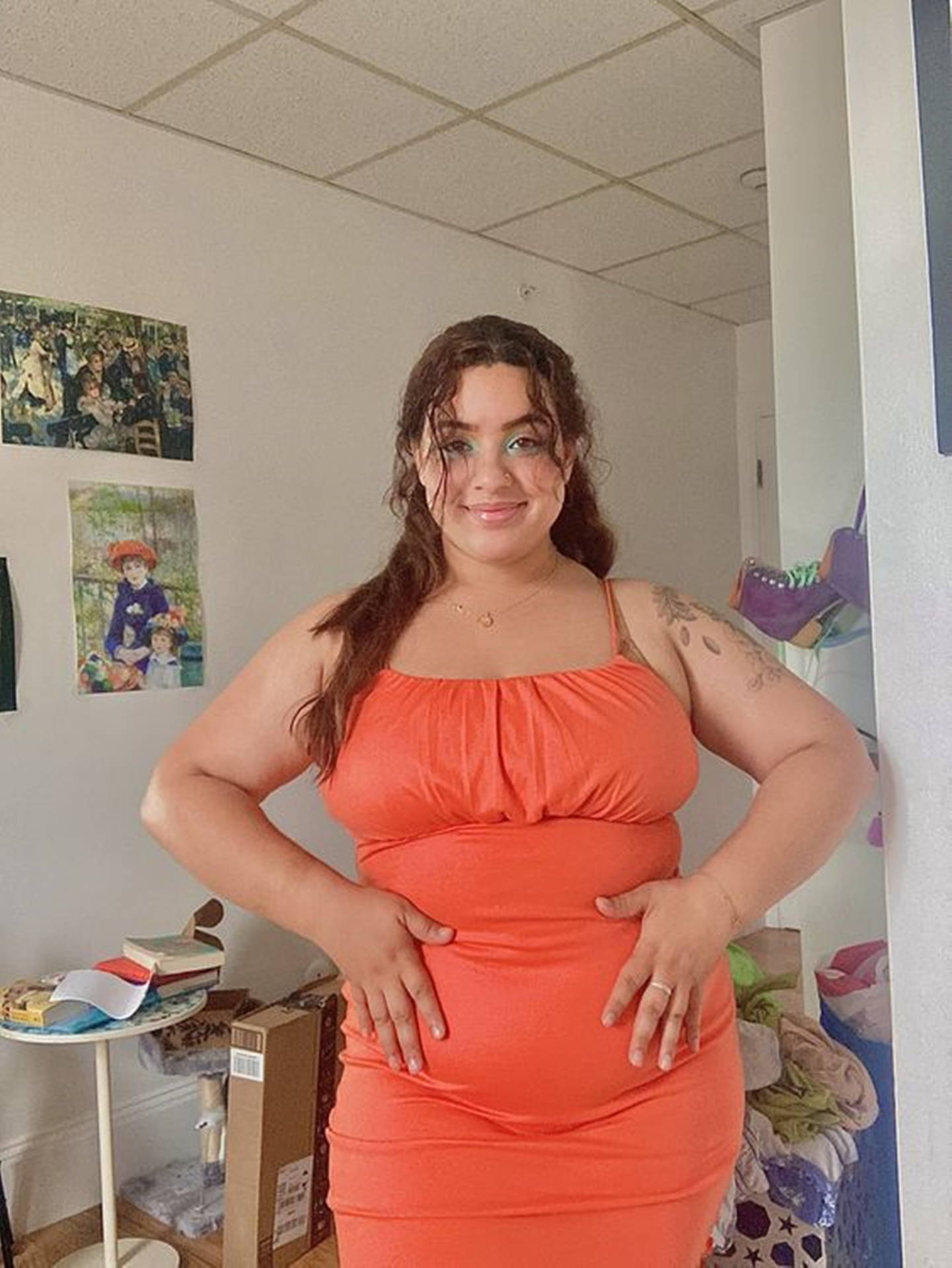 身穿橙色連衣裙的女性在室內雙手叉腰擺姿勢。