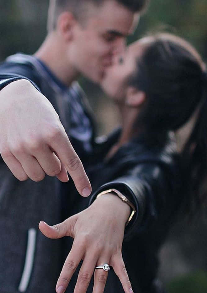 男子指向女子手指上的訂婚戒指，他們正在接吻。