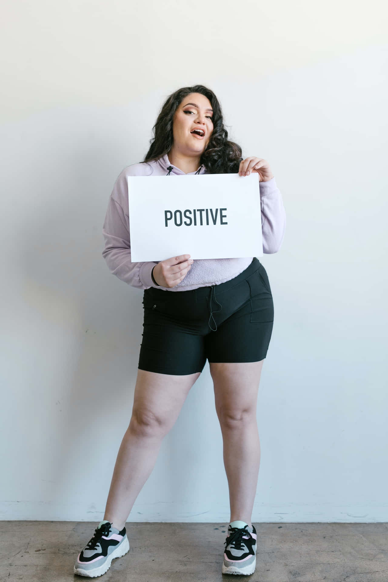 一位開心的女性在室內舉著寫有「positive」的標語牌。
