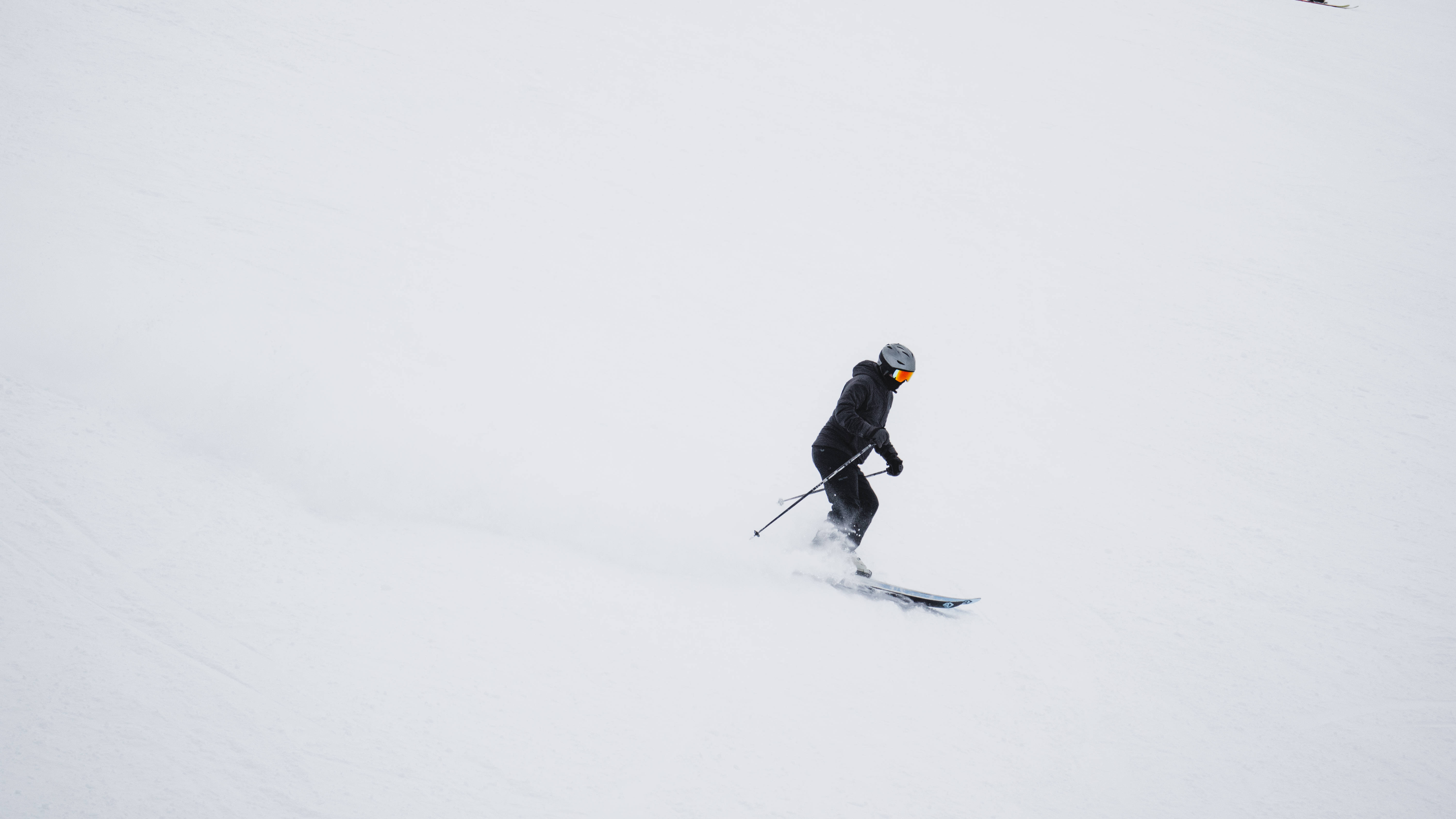 穿黑色裝束的滑雪者 壁紙 — 一名穿著黑色裝備的滑雪者在多雲的天空下，在廣闊的雪坡上劃過新鮮的粉雪。