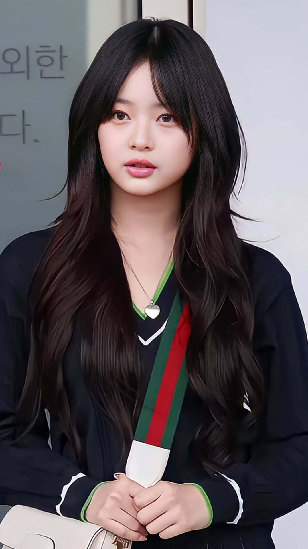 穿黑色襯衫的年輕女子 壁紙 — 一位長黑髮的年輕女性穿著帶有綠色和紅色條紋的黑色外套，手持一個白色手袋。