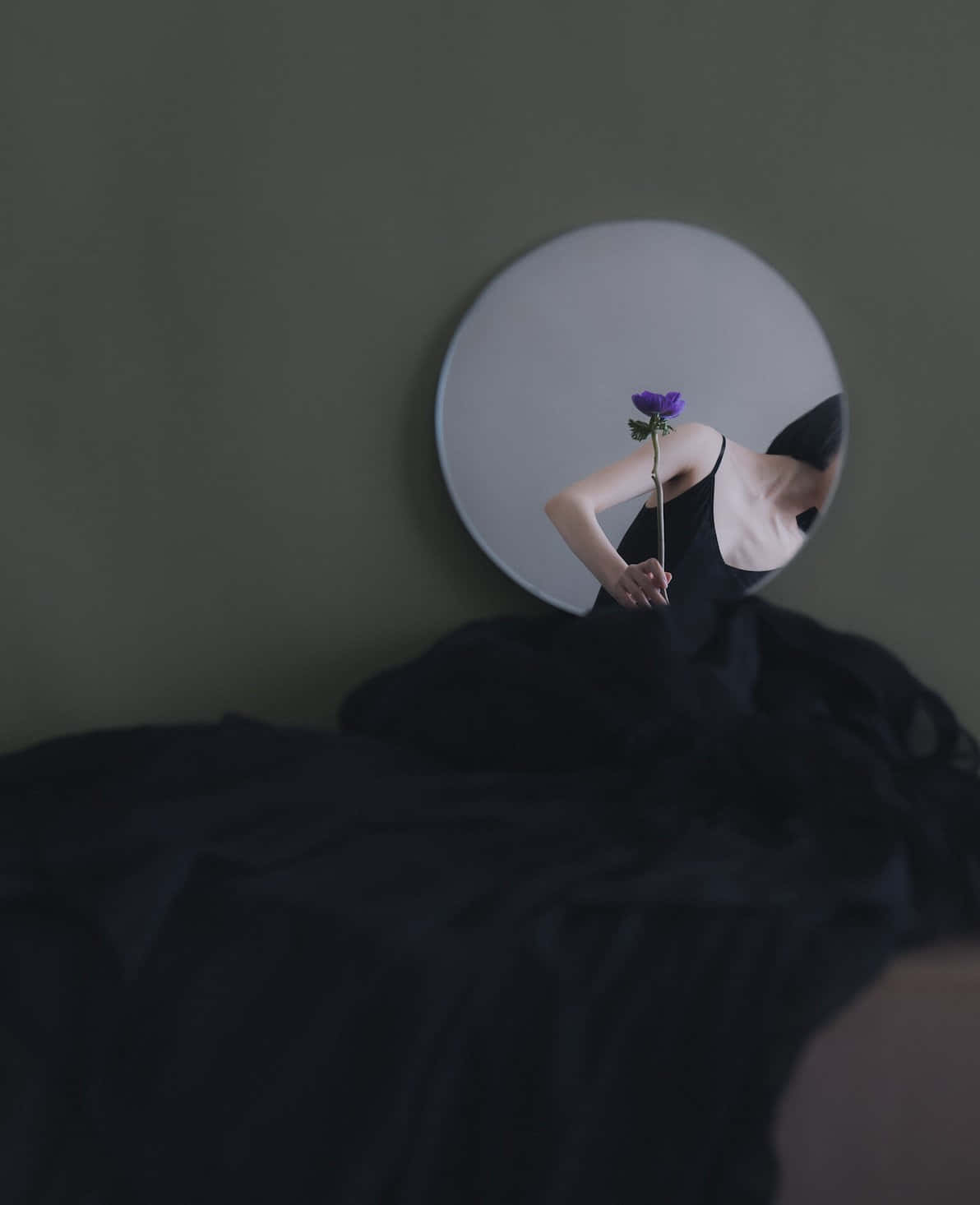 人拿著紫色花映照在圓鏡中，背景是綠色牆壁。