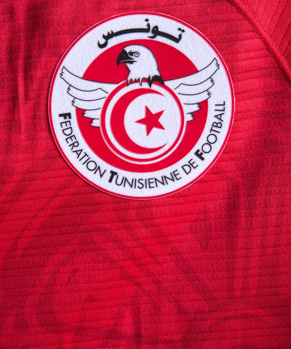 Logo 桌布 壁紙 — 突尼斯國家足球協會會徽在帶有紋理的紅色運動球衣上的特寫。