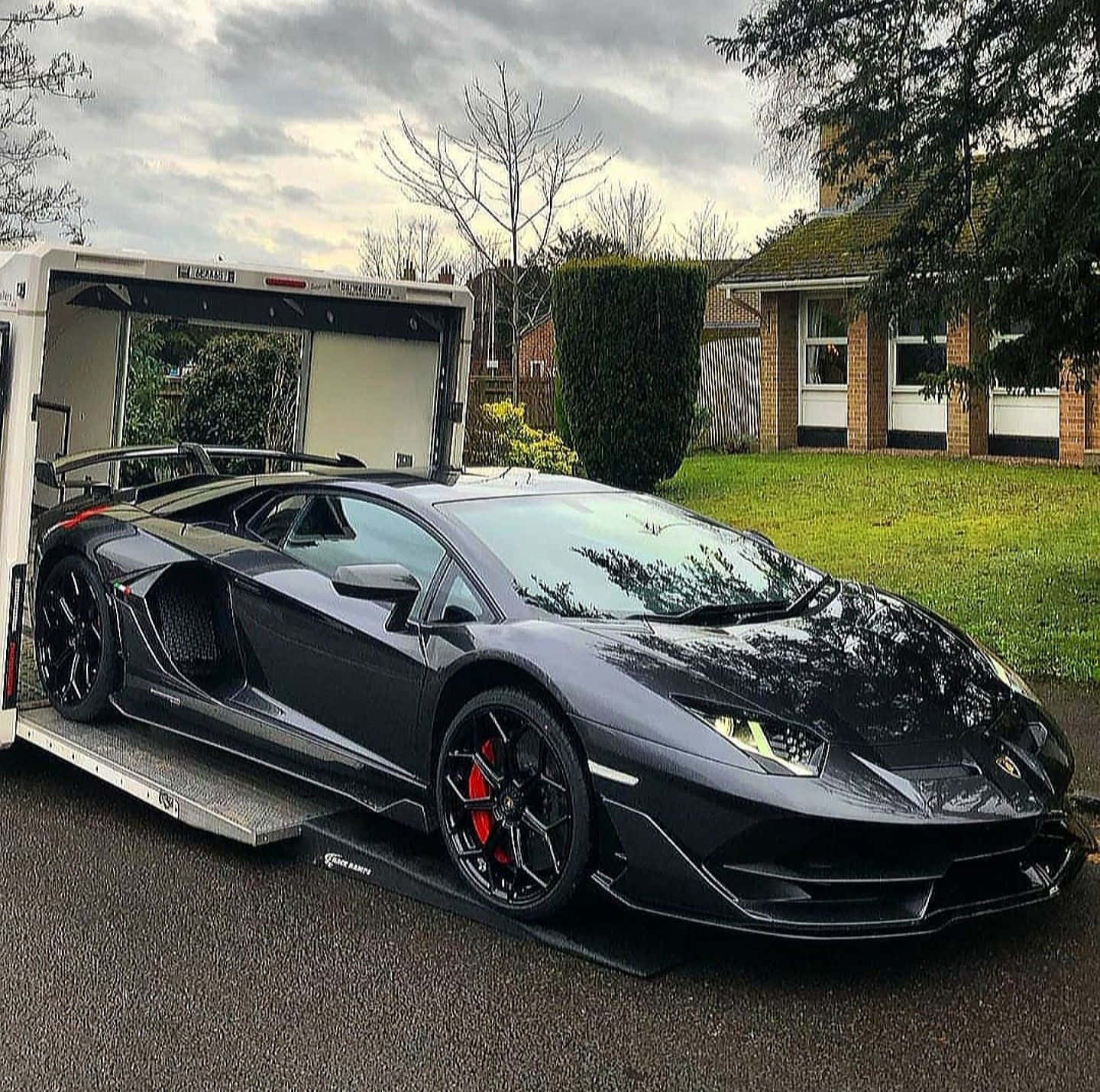 突破終點線 壁紙 — 一架型格啞黑色林寶堅尼Aventador停泊在郊區車道的拖車上，天空密雲。