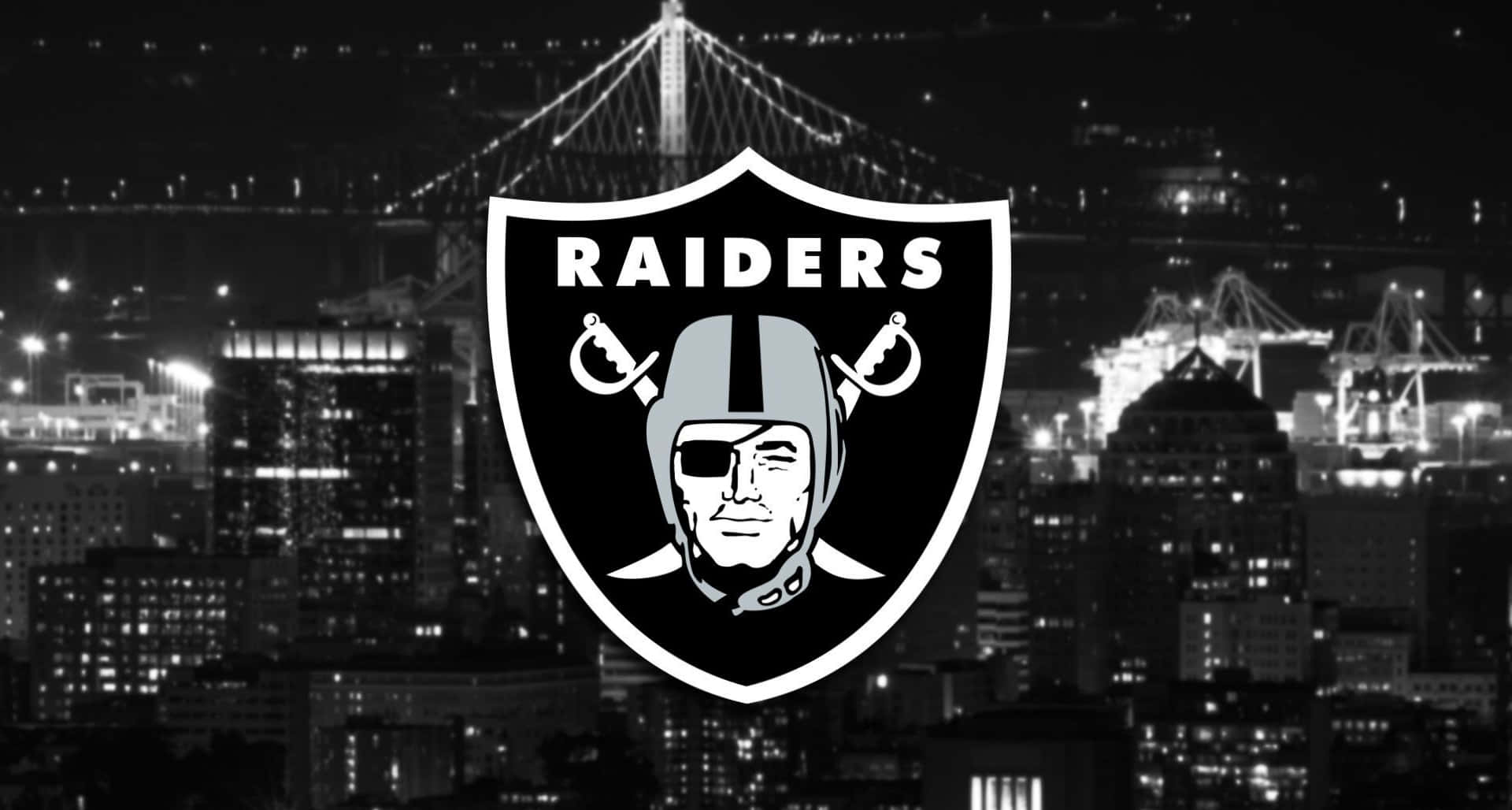 Raiders 標誌覆蓋在夜景城市上，有亮燈的橋樑和起重機。 — 掠奪者 壁紙