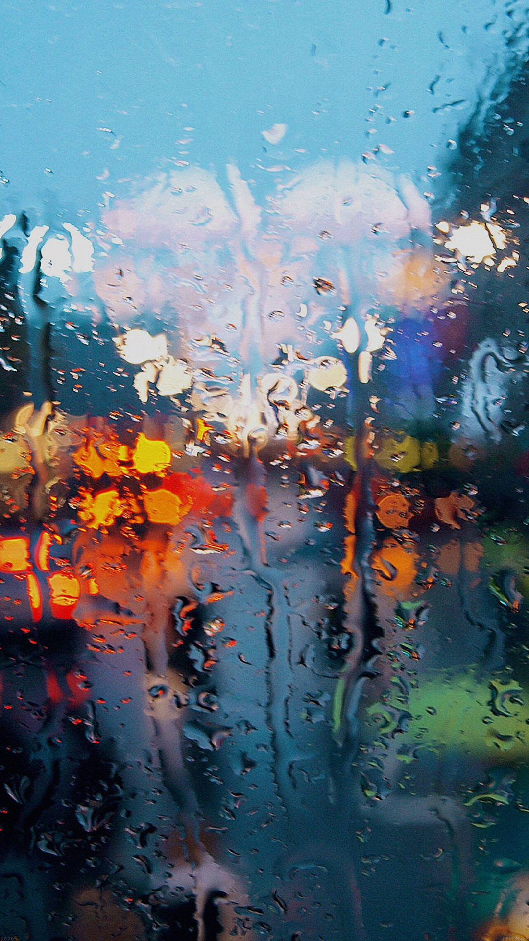 雨滴模糊了夜晚濕窗戶上色彩繽紛的城市燈光。