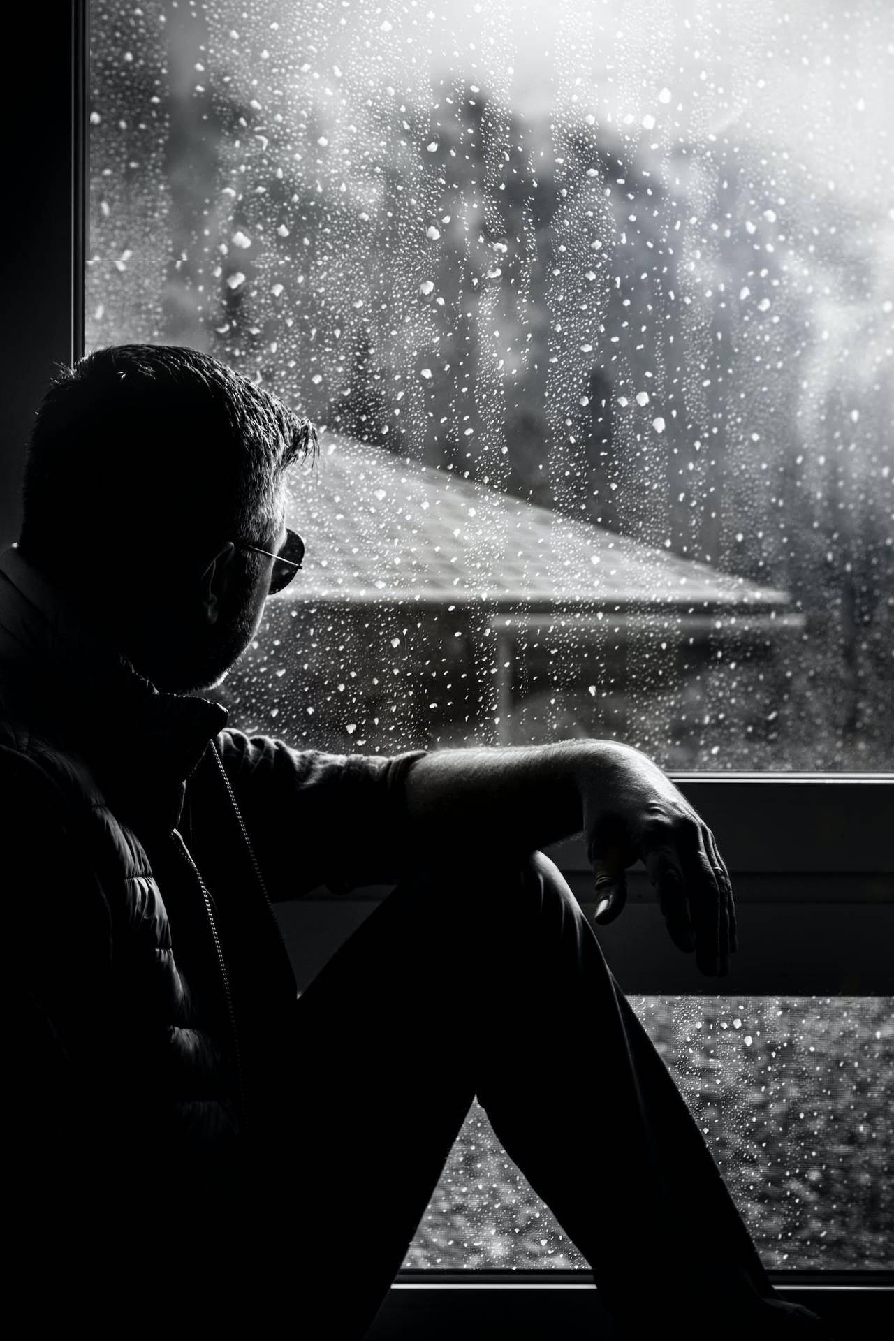 剪影男人坐在雨窗邊看著雪景