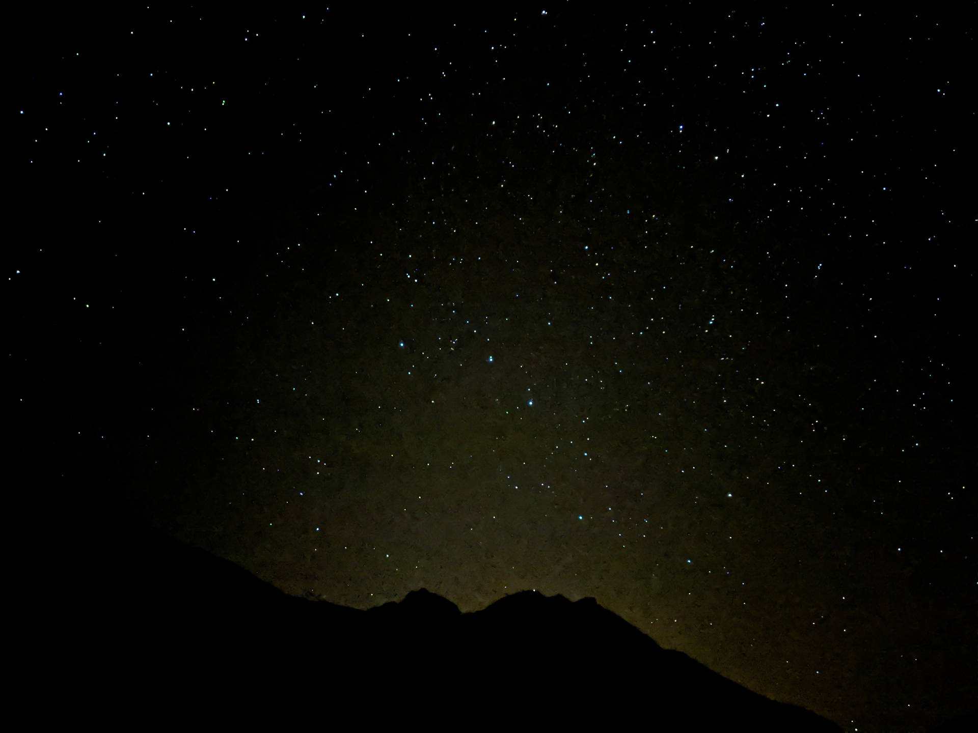 在繁星點點的夜空下，黑暗的山脈輪廓映襯著溫暖的地平線光芒。