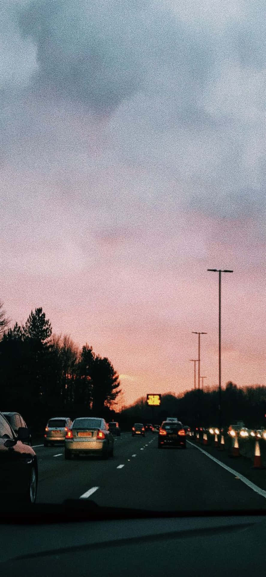 黃昏時分高速公路上的汽車，粉紅和紫色的天空和烏雲。