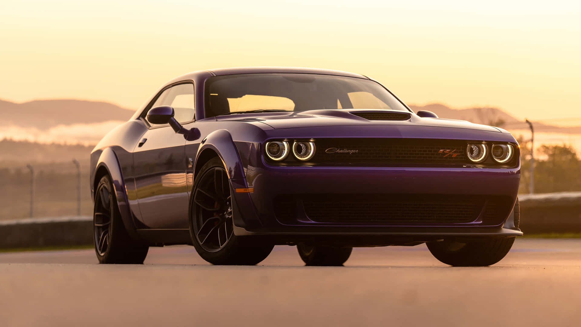 紫色Dodge Challenger SRT Hellcat喺日落時分嘅賽道上，背景有山丘。