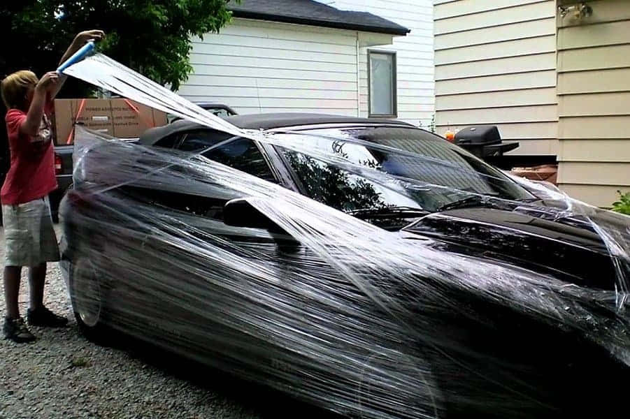 孩子在車道上用膠膜包裹黑色跑車。
