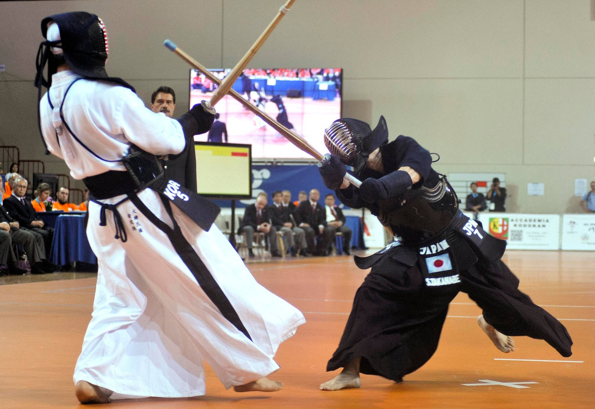 第15屆義大利劍道錦標賽激烈對決 壁紙 — 兩名全副武裝的劍道鬥士在木製道場地板上激烈交鋒，觀眾在旁觀看。