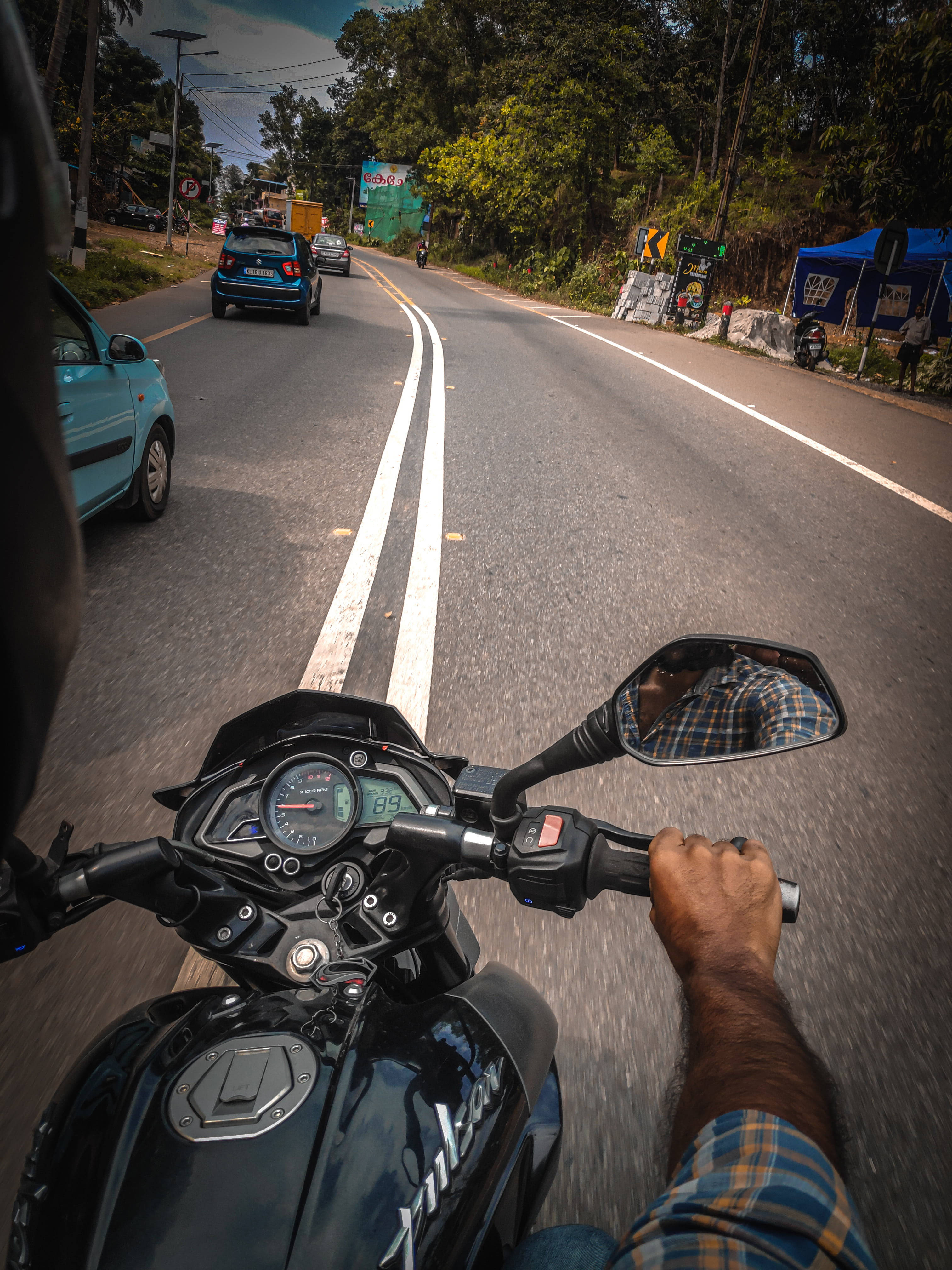 道路 桌布 壁紙 — 第一人稱視角，一名騎士握著黑色電單車的把手，在蜿蜒的瀝青路上飛馳，路邊有樹木和攤檔。