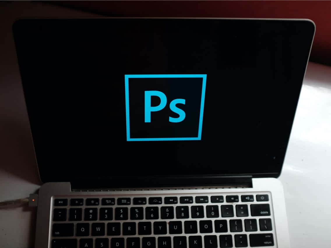 筆記型電腦螢幕上的 Photoshop 標誌 壁紙 — 一部手提電腦在黑色屏幕上顯示發光的藍色Adobe Photoshop標誌，下方可見鍵盤。