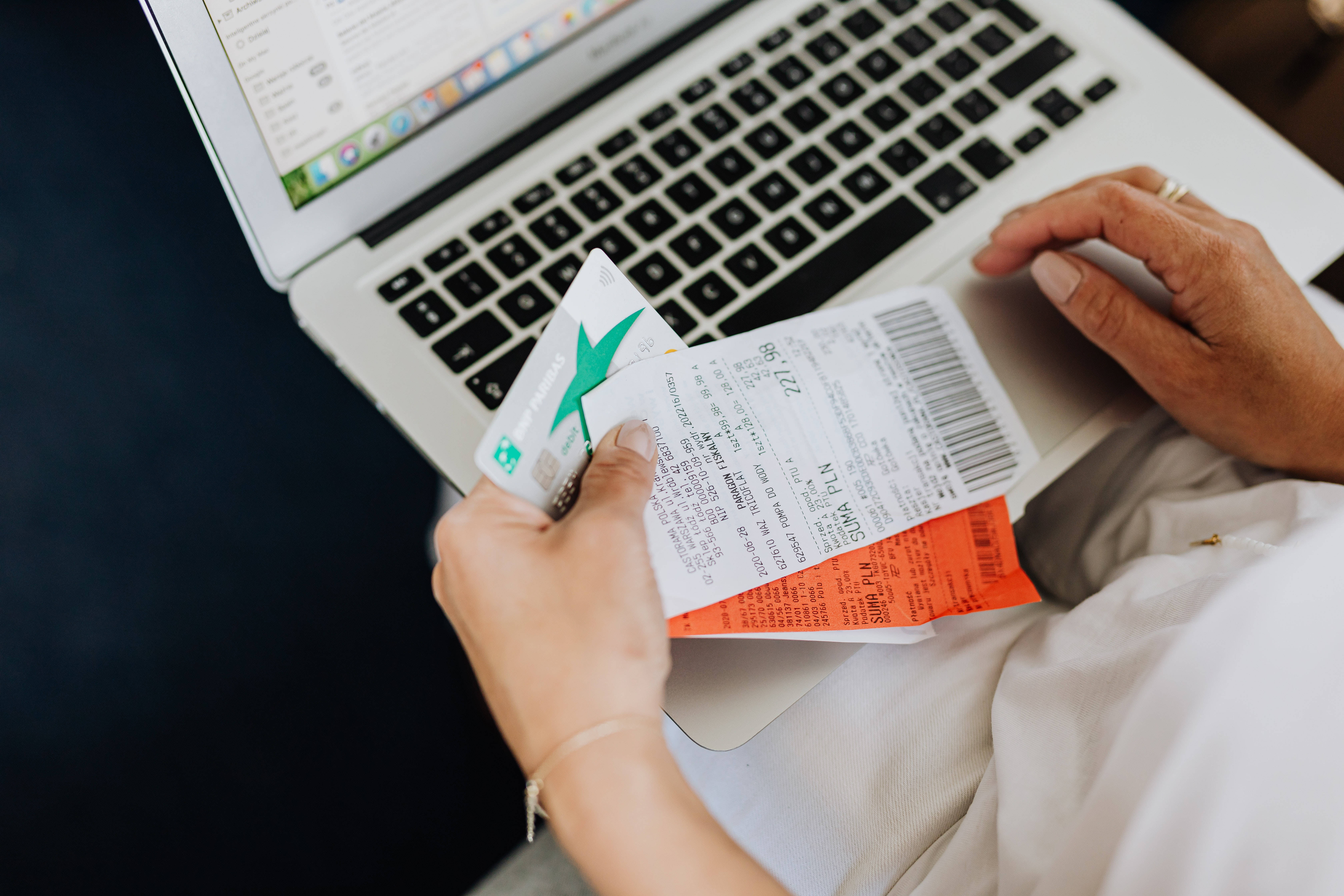 筆電與收據 壁紙 — 特寫雙手拿著旅行機票和信用卡在打開的筆記本電腦鍵盤上方。