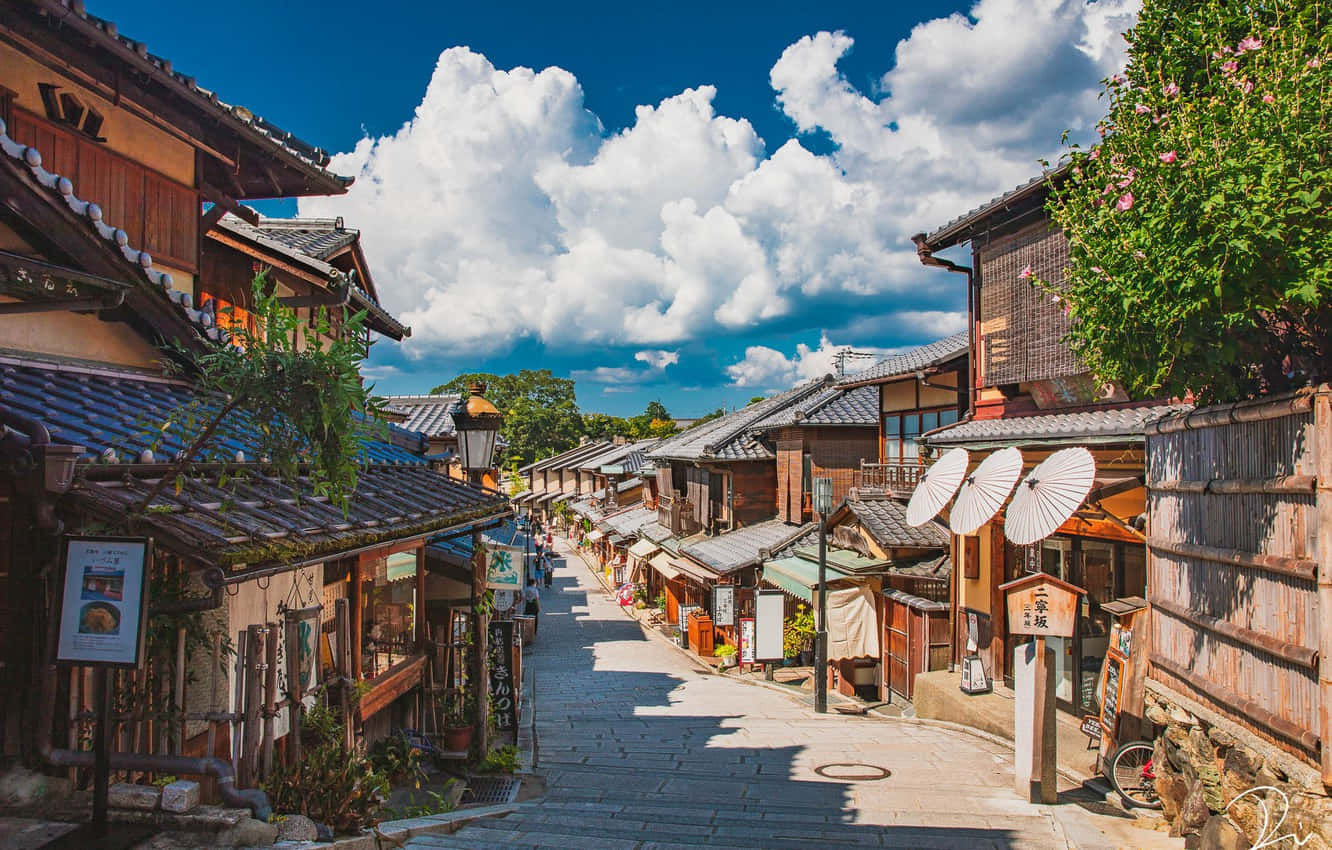 箱根與忍野八海湖畔，環繞日本阿尔卑斯山的壯麗風景 壁紙 — 一條陽光明媚的鵝卵石街道，兩旁是傳統木建築和紙傘，上方是明亮的藍天和蓬鬆的白雲。