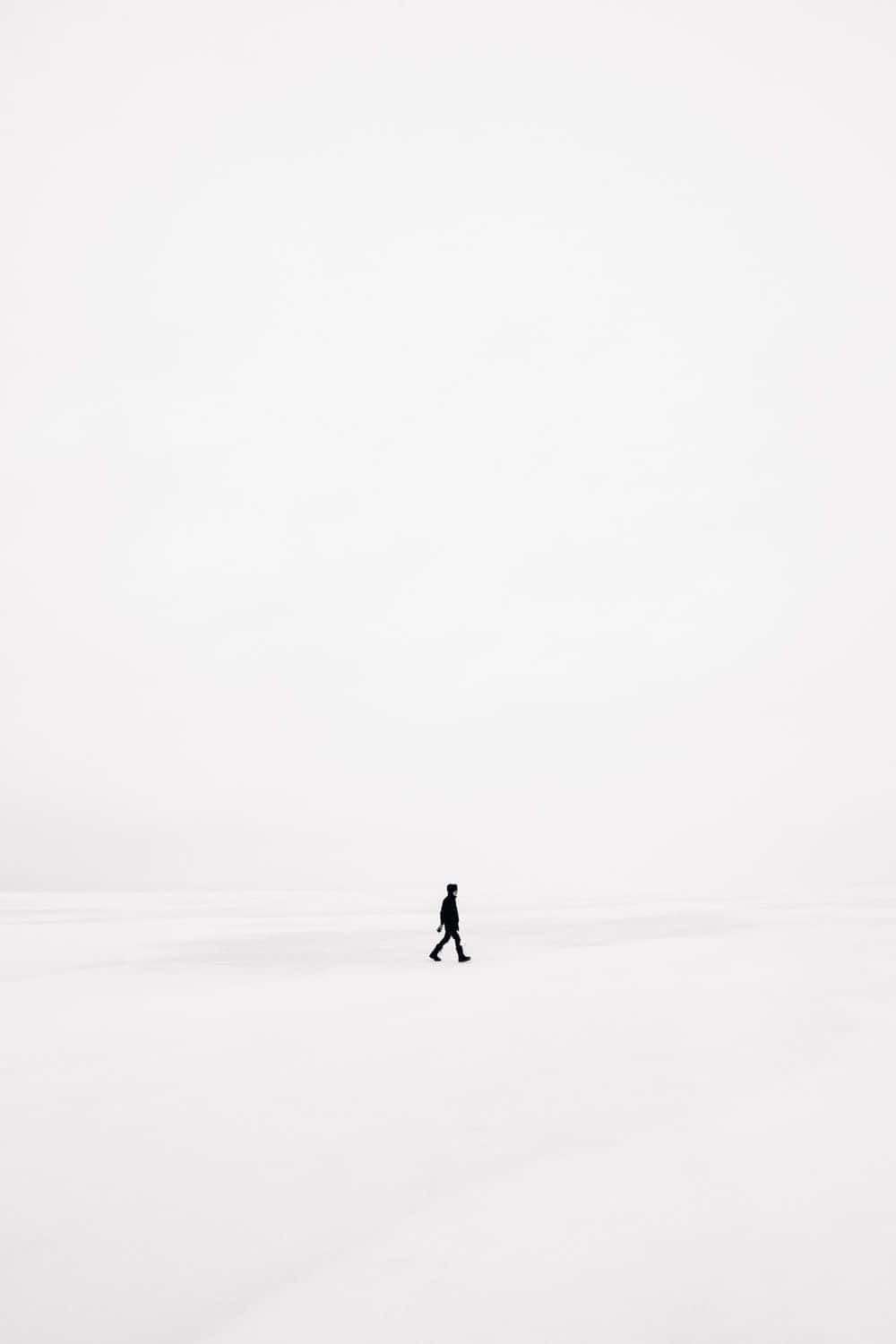 一個人在灰色天空下獨自走過廣闊的雪地。