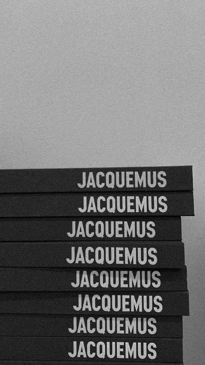 一堆黑色書籍，上面有白色 Jacqumus 文字，背景為灰色。