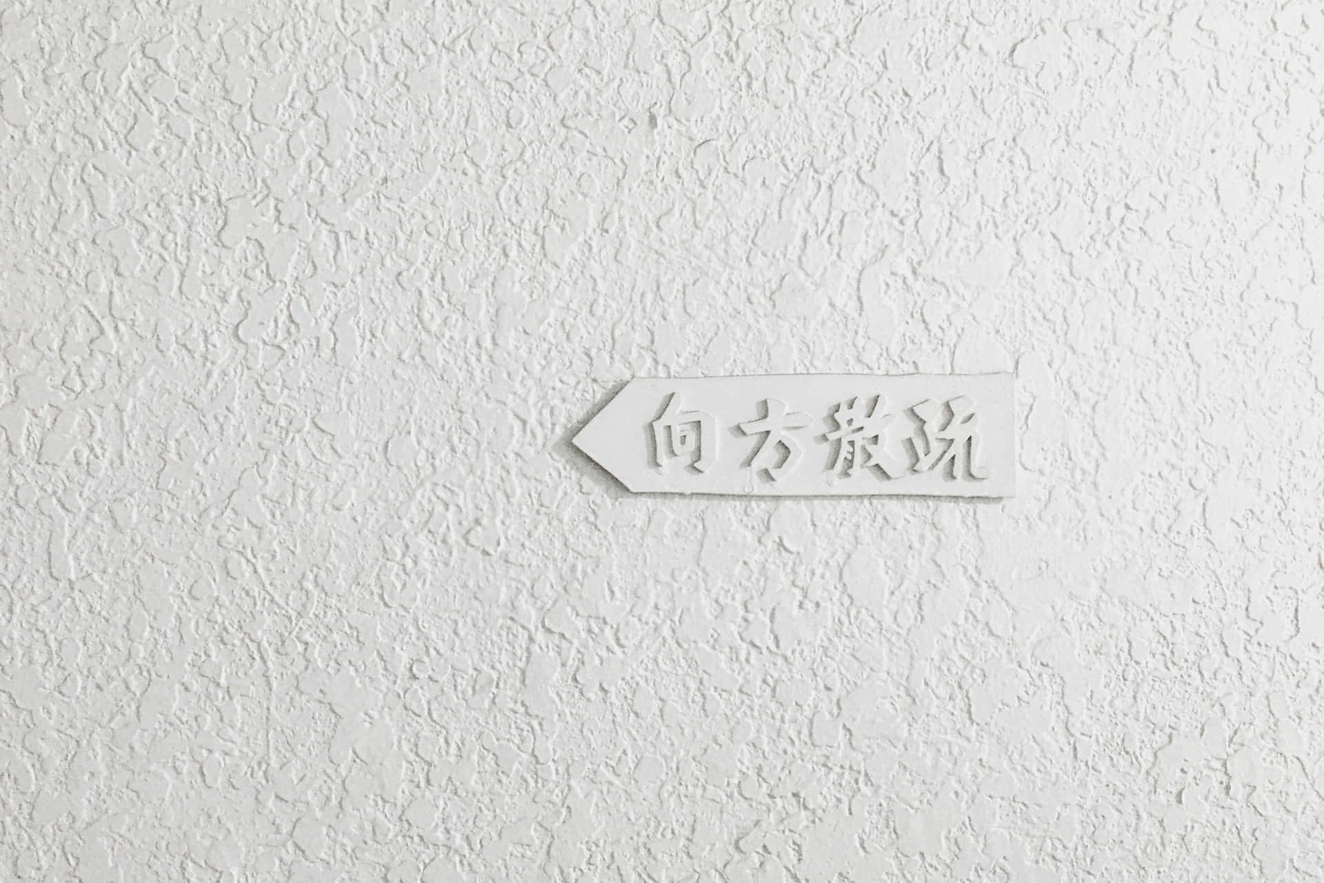 帶有日文文字的白色方向標誌，位於有紋理的牆上。