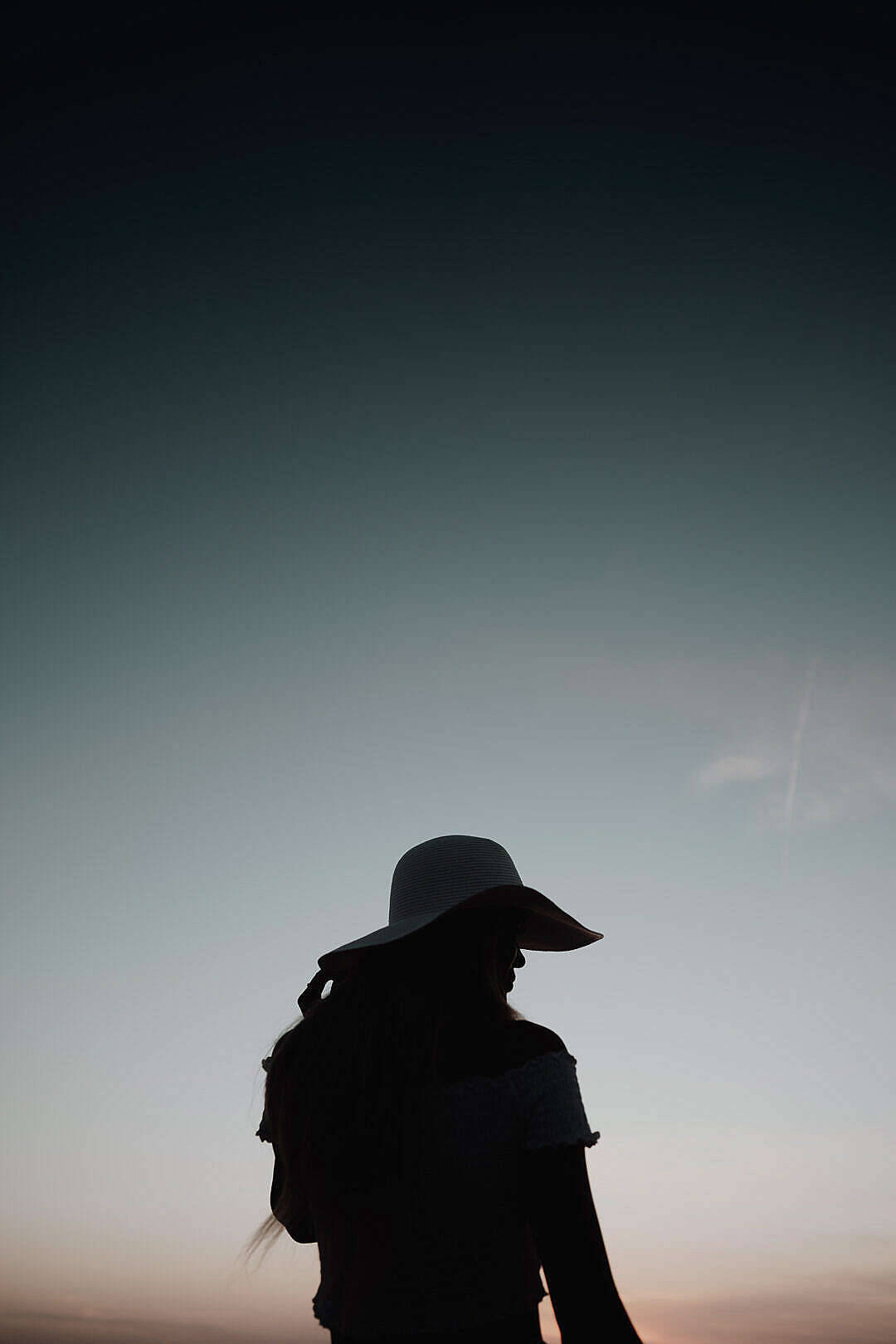 簡約暗黑風格女子夕陽 壁紙 — 戴闊邊帽的人凝視著黃昏漸變天空的剪影。