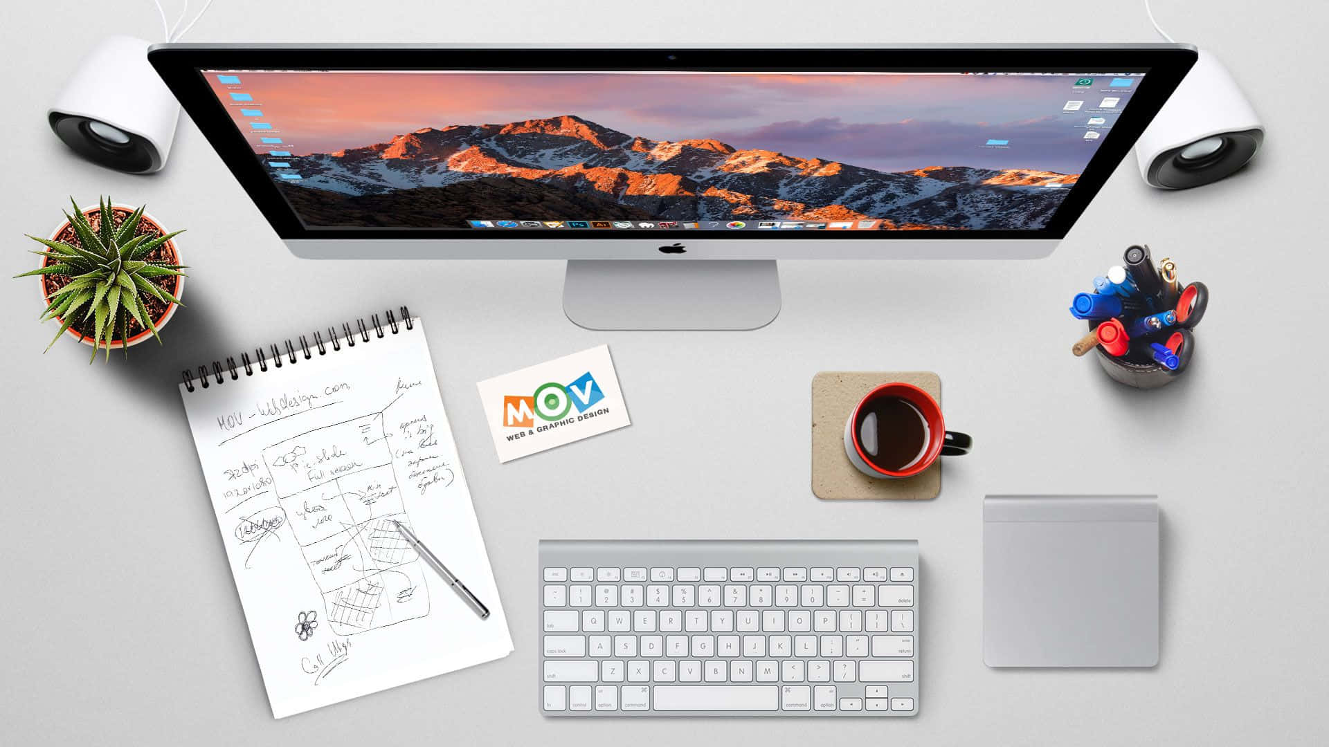 Website 桌布 壁紙 — 簡約白色桌面設置，iMac 顯示雪山日落壁紙，周圍有咖啡、筆記本和揚聲器。