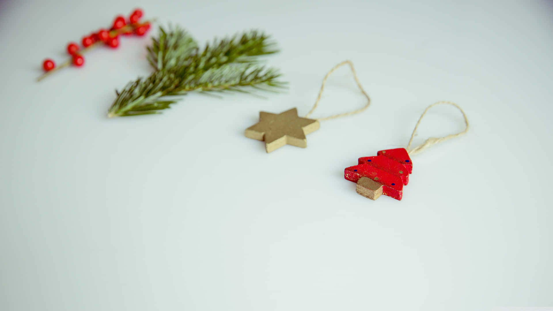 Vintage Christmas 桌布 壁紙 — 簡約節日裝飾，以紅色漿果、綠色松枝和木製星星及樹木裝飾品點綴在潔白表面上。
