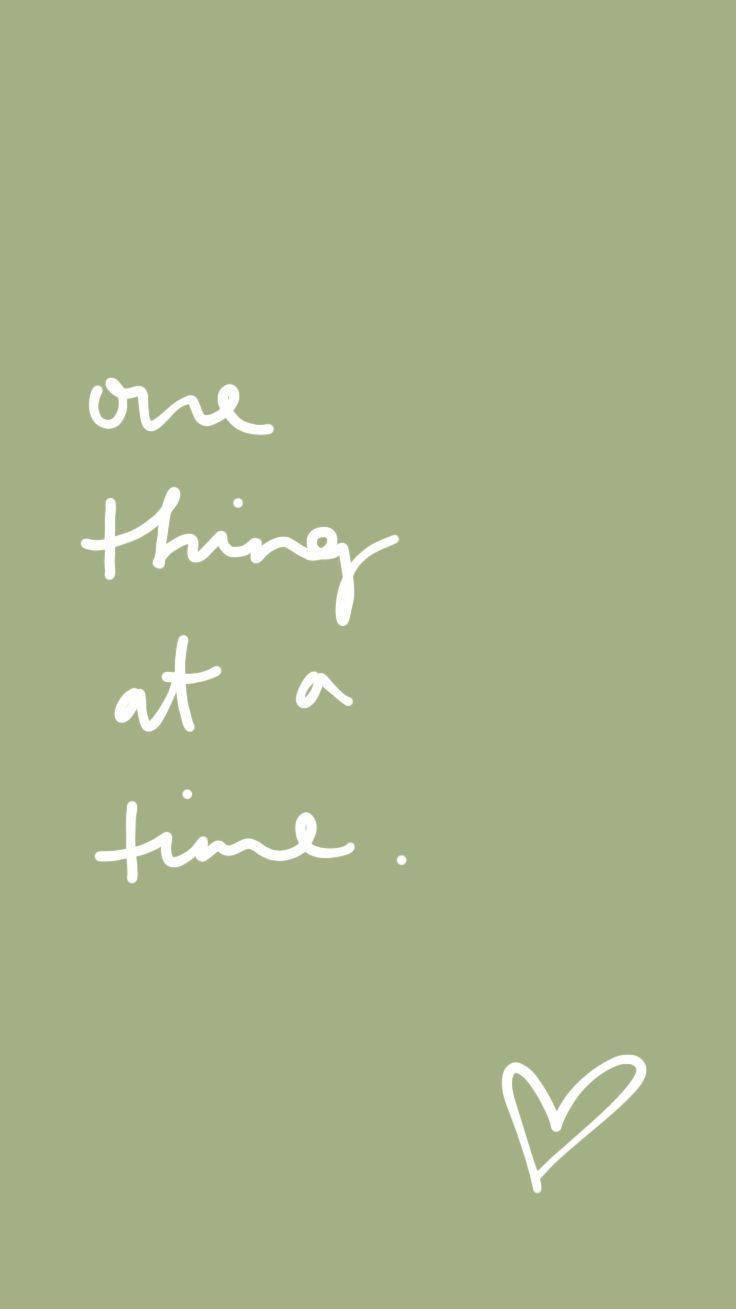 白色手寫語錄「one thing at a time」在鼠尾草綠色背景上，附小心形。